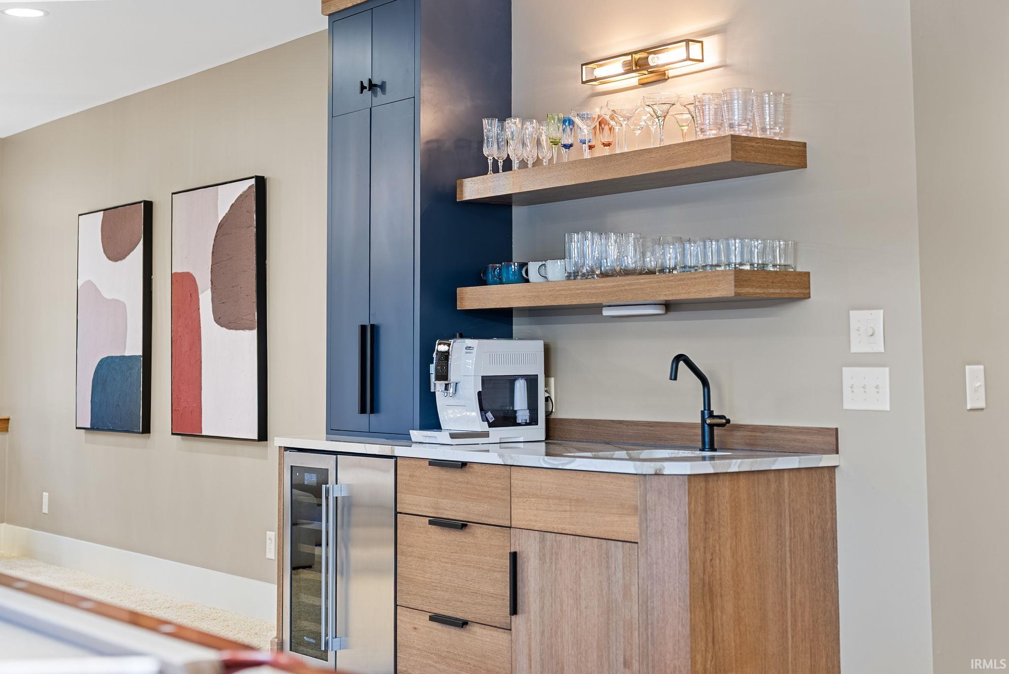 Indoor wet bar with modern cabinets, open shelves, wine cooler, and light stone counters