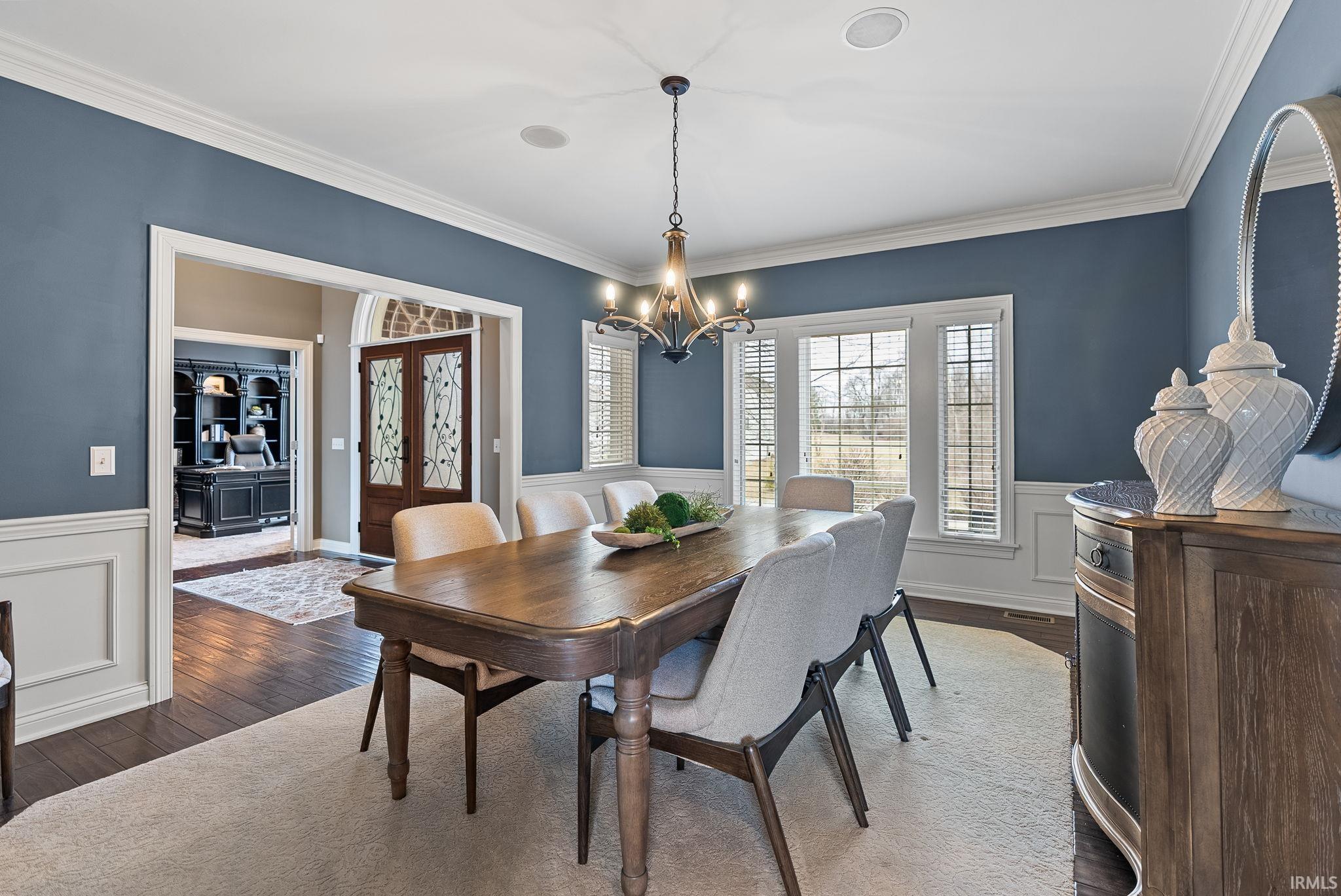 Dining room featuring dark wood-type flooring, a chandelier, a wainscoted wall, a decorative wall, and crown molding