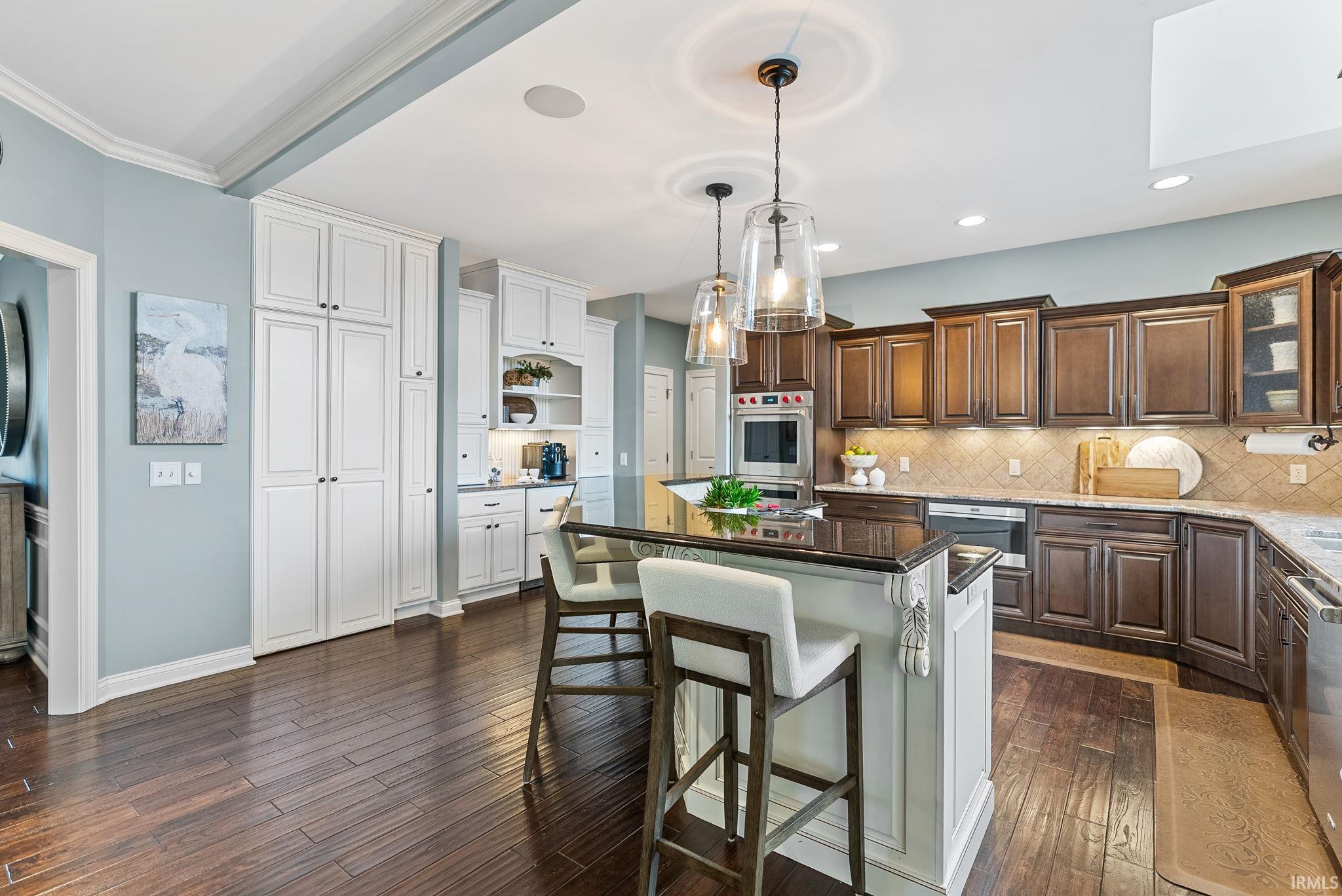 Dual tone kitchen with a breakfast bar, a kitchen island, dark stone counters, decorative light fixtures, and backsplash