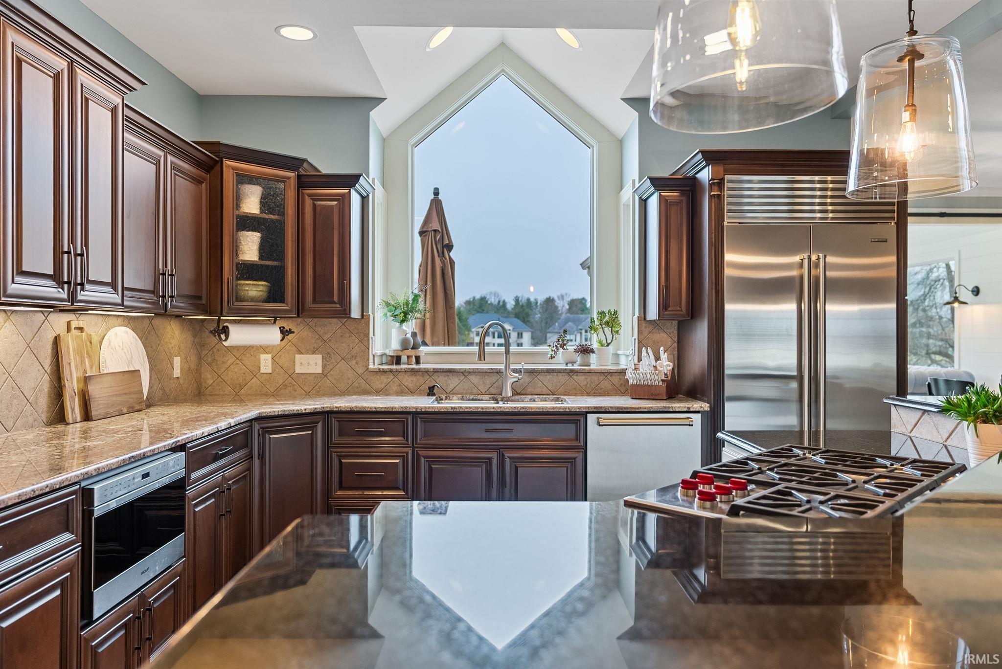 Kitchen featuring stainless steel appliances, dark stone countertops, glass fronted cabinets, tasteful backsplash, and dark wood finish cabinetry