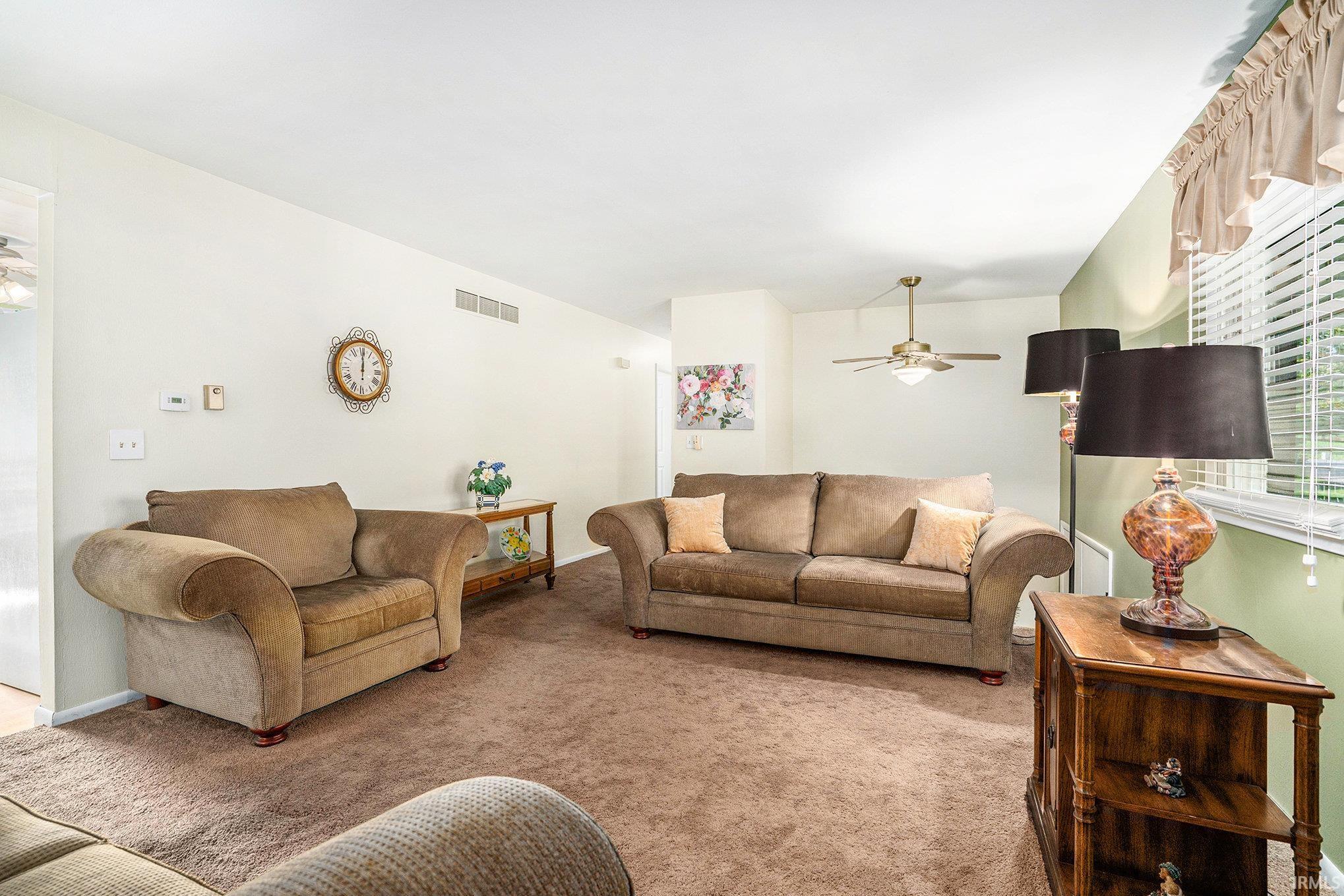 Carpeted living room featuring ceiling fan and baseboards