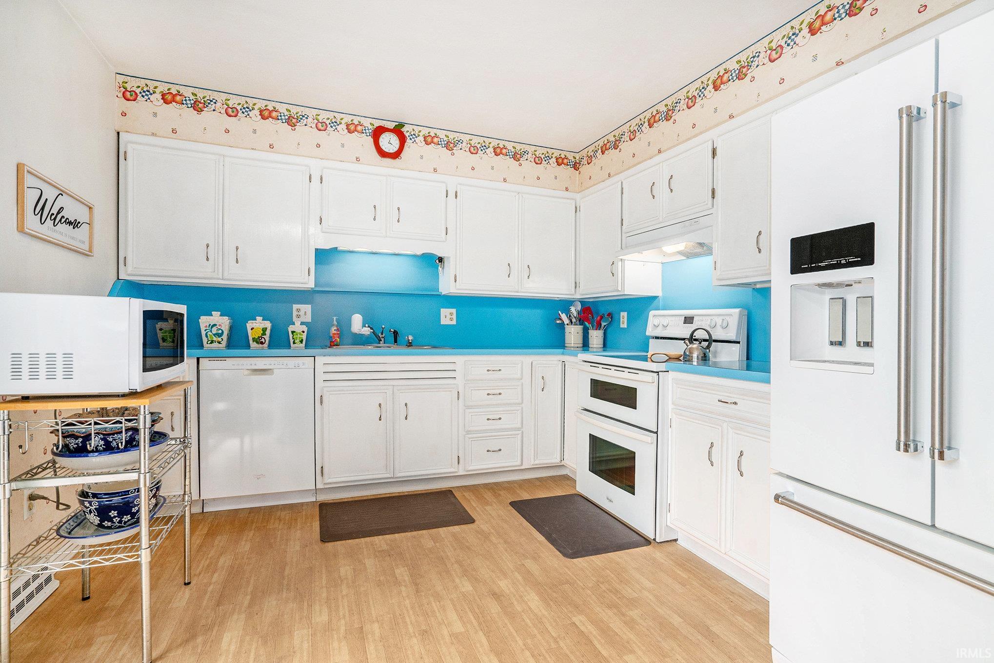 Kitchen featuring white appliances, light wood finished floors, white cabinetry, and light countertops