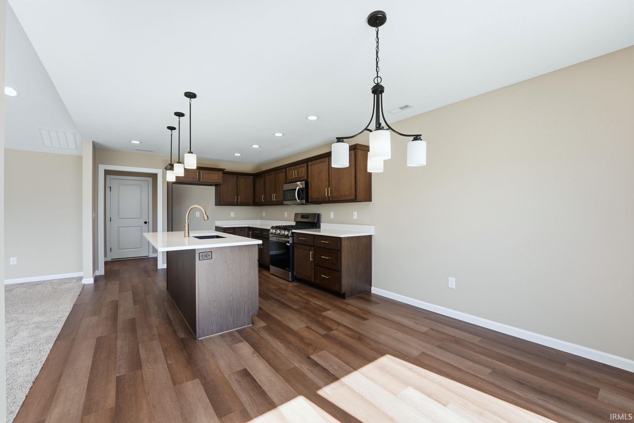 Kitchen featuring stainless steel appliances, a kitchen island with sink, dark wood-style floors, dark wood finish cabinets, and a chandelier