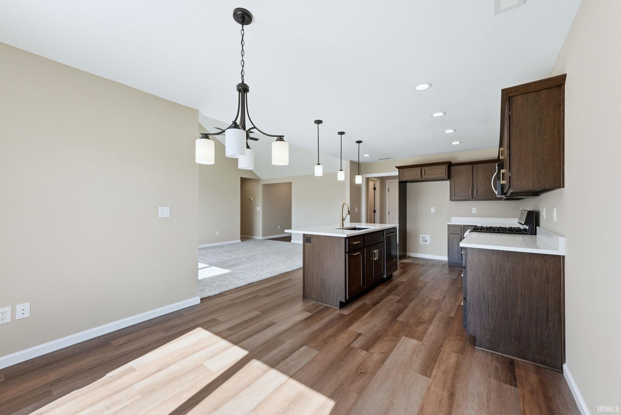 Kitchen with an island with sink, dark wood finish cabinetry, open floor plan, and dark wood finished floors