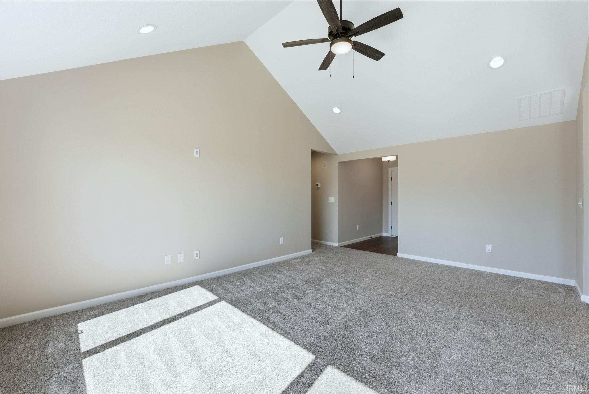 Empty room featuring dark carpet, a ceiling fan, a high ceiling, and recessed lighting