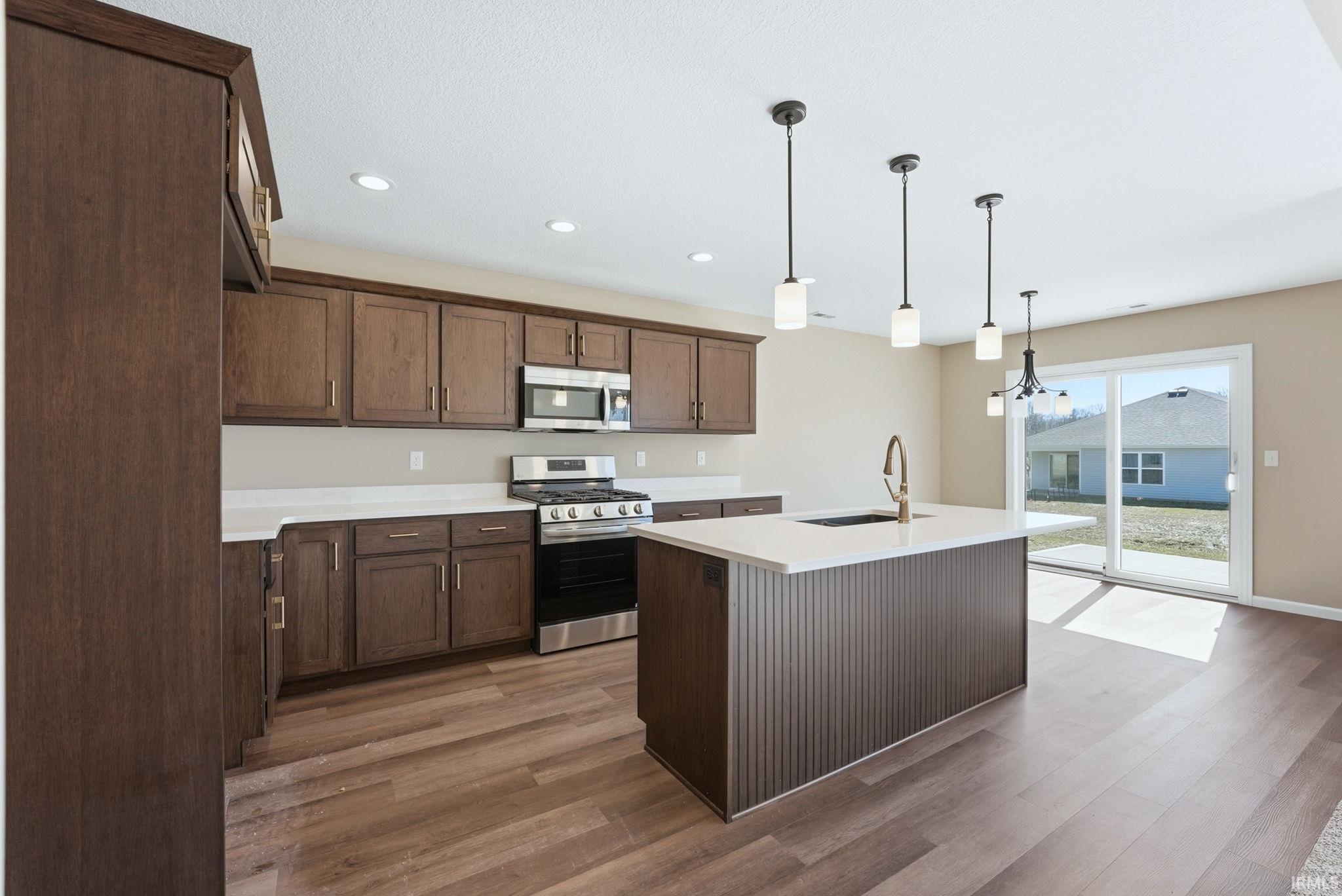 Kitchen featuring stainless steel appliances, a kitchen island with sink, suspended lighting, and light wood finished floors