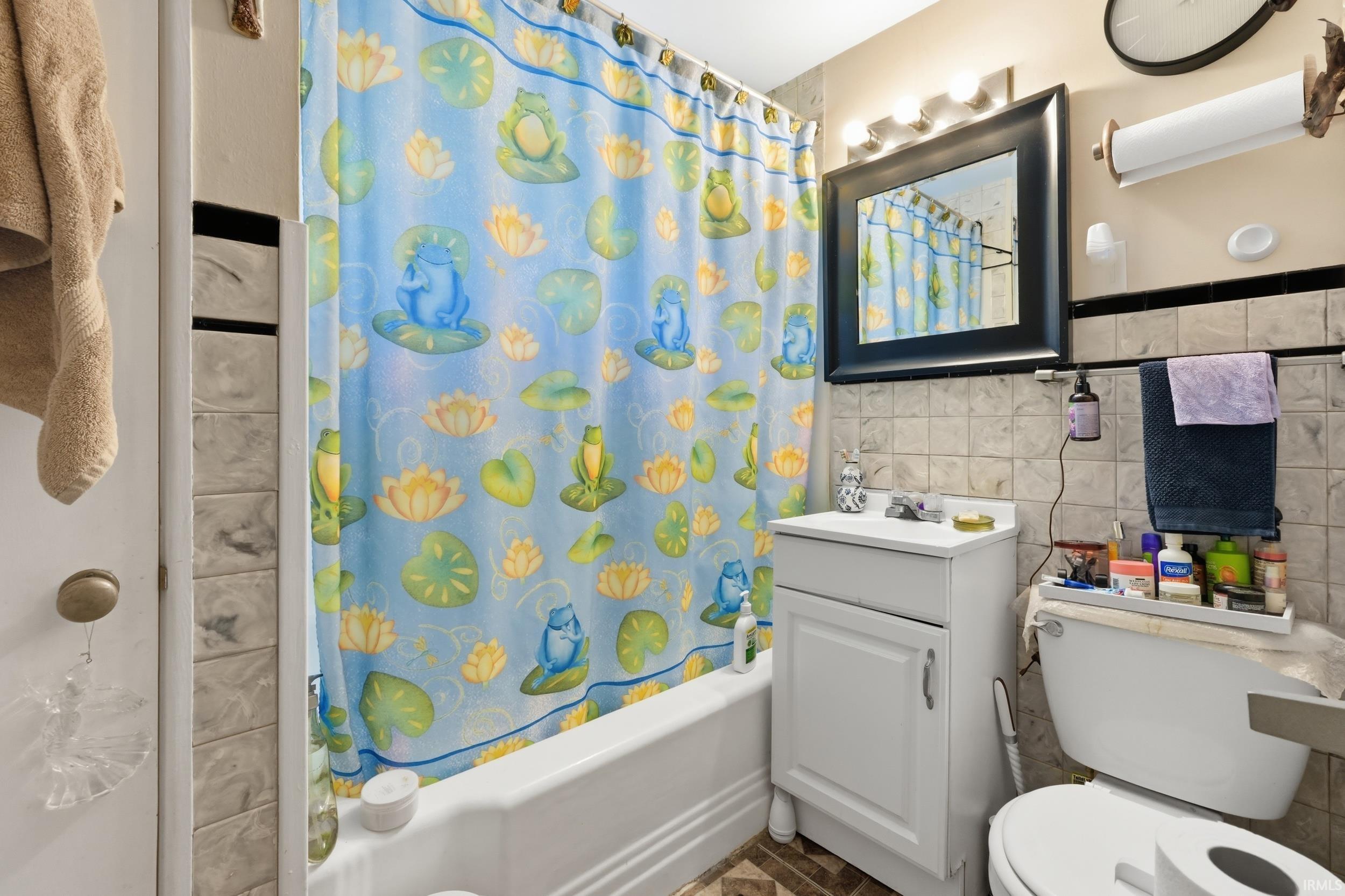 Bathroom featuring tile walls, vanity, shower / bath combination with curtain, and wainscoting