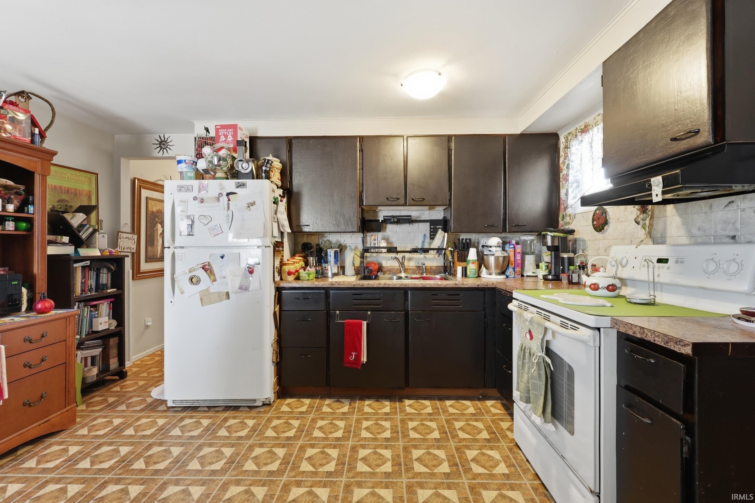 Kitchen with white appliances, dark wood finish cabinets, light countertops, light flooring, and backsplash