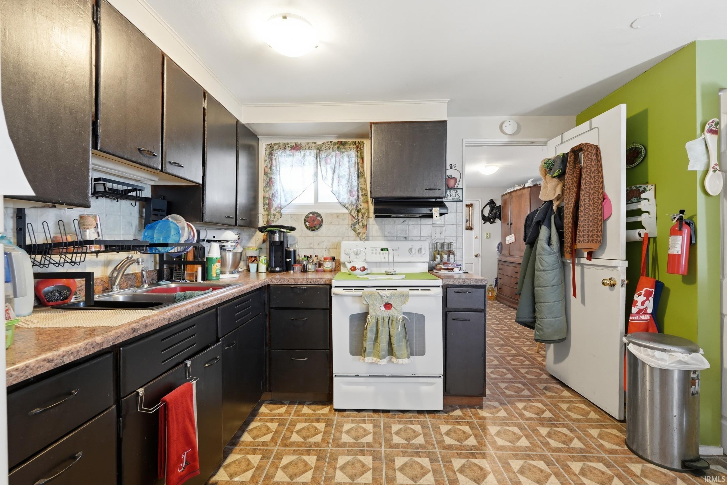 Kitchen featuring white electric range, light flooring, light countertops, backsplash, and dark wood finish cabinets