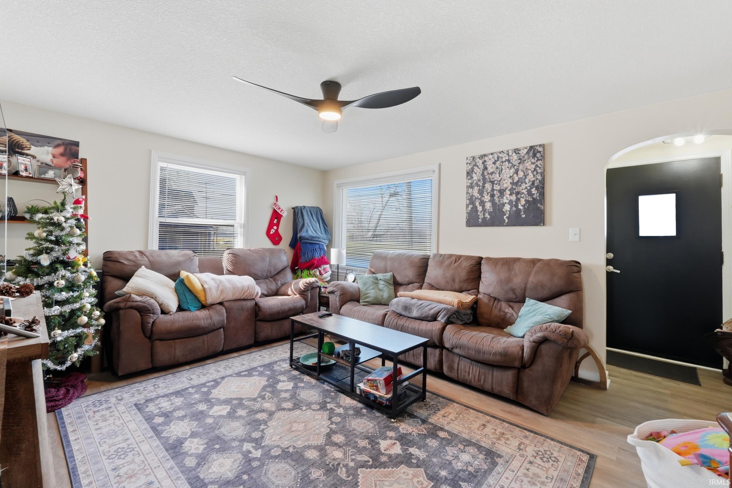 Living room with ceiling fan, light wood finished floors, and arched walkways