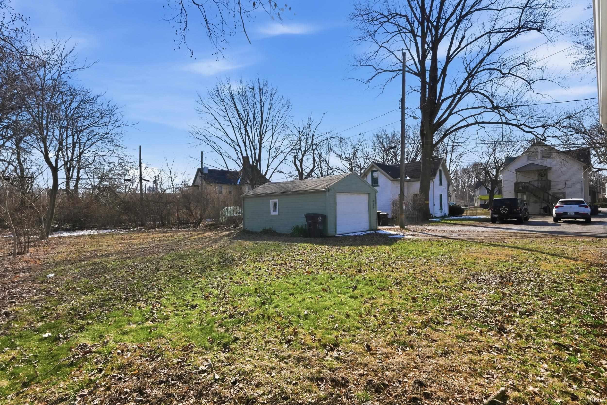 View of grassy yard featuring a detached garage, an outbuilding, and a residential view