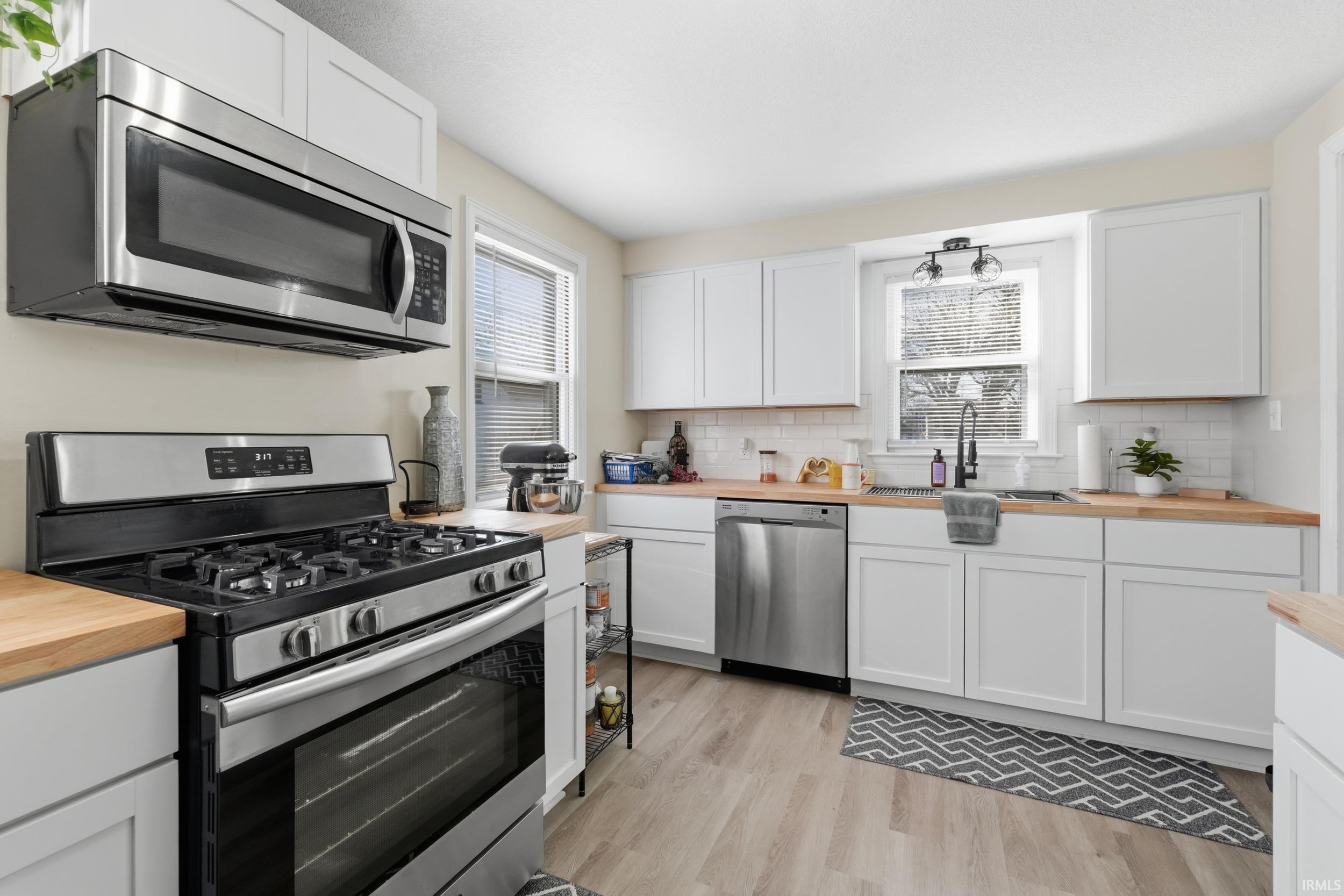 Kitchen featuring wood counters, stainless steel appliances, white cabinets, and light wood-style flooring