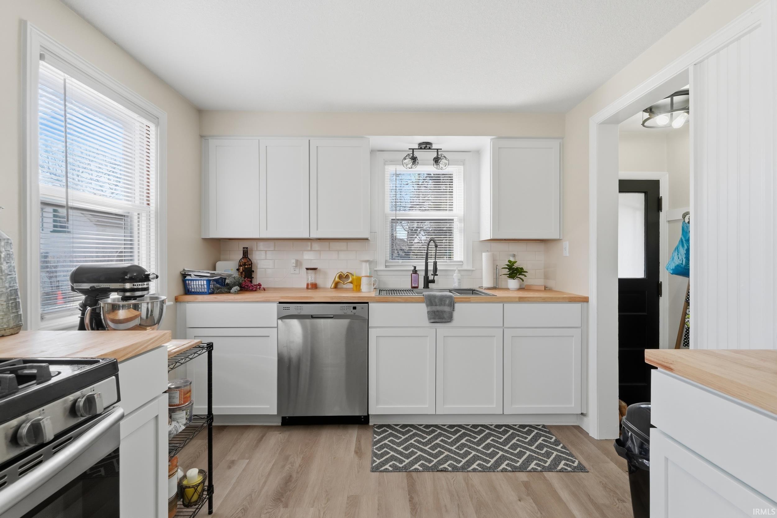 Kitchen featuring white cabinetry, butcher block countertops, light wood-style floors, and dishwasher