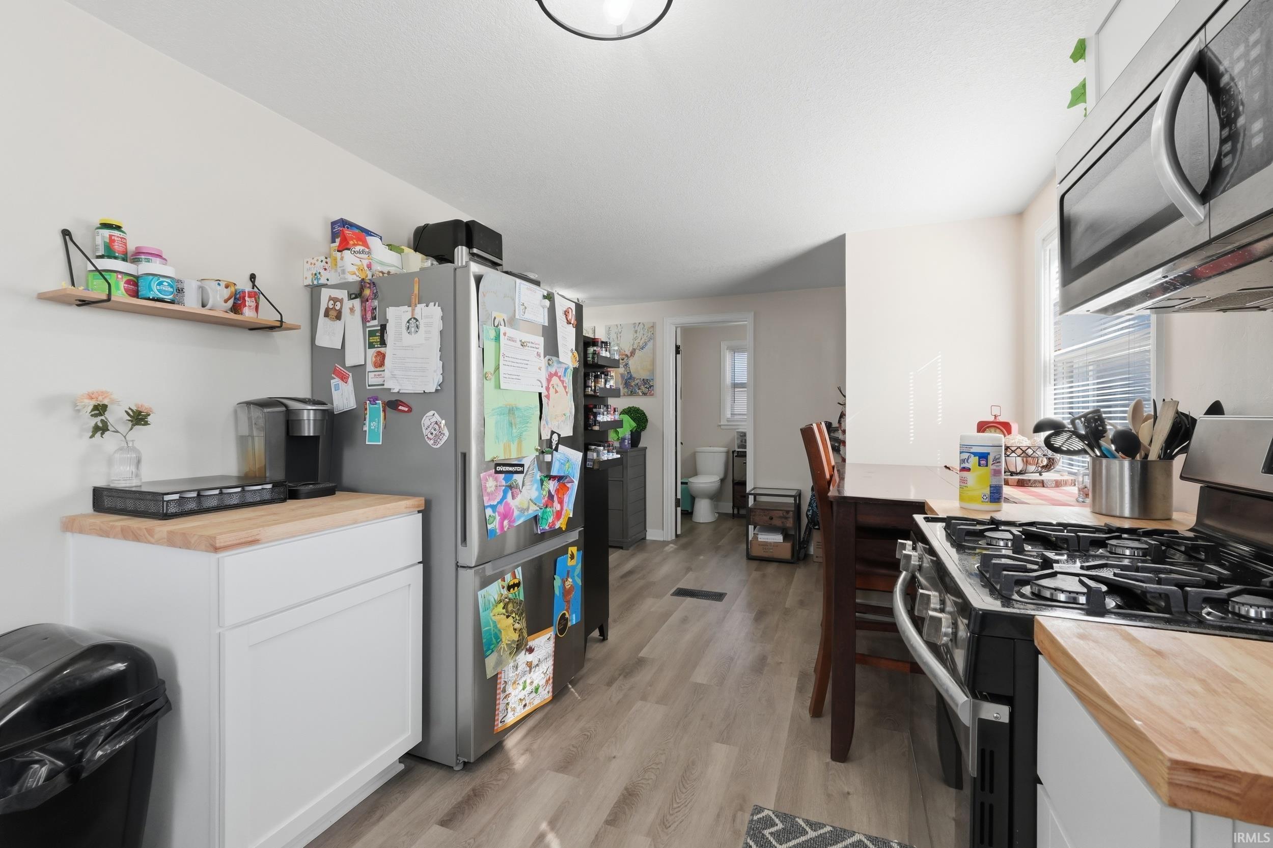 Kitchen featuring wood counters, stainless steel appliances, white cabinets, light wood-style flooring, and open shelves