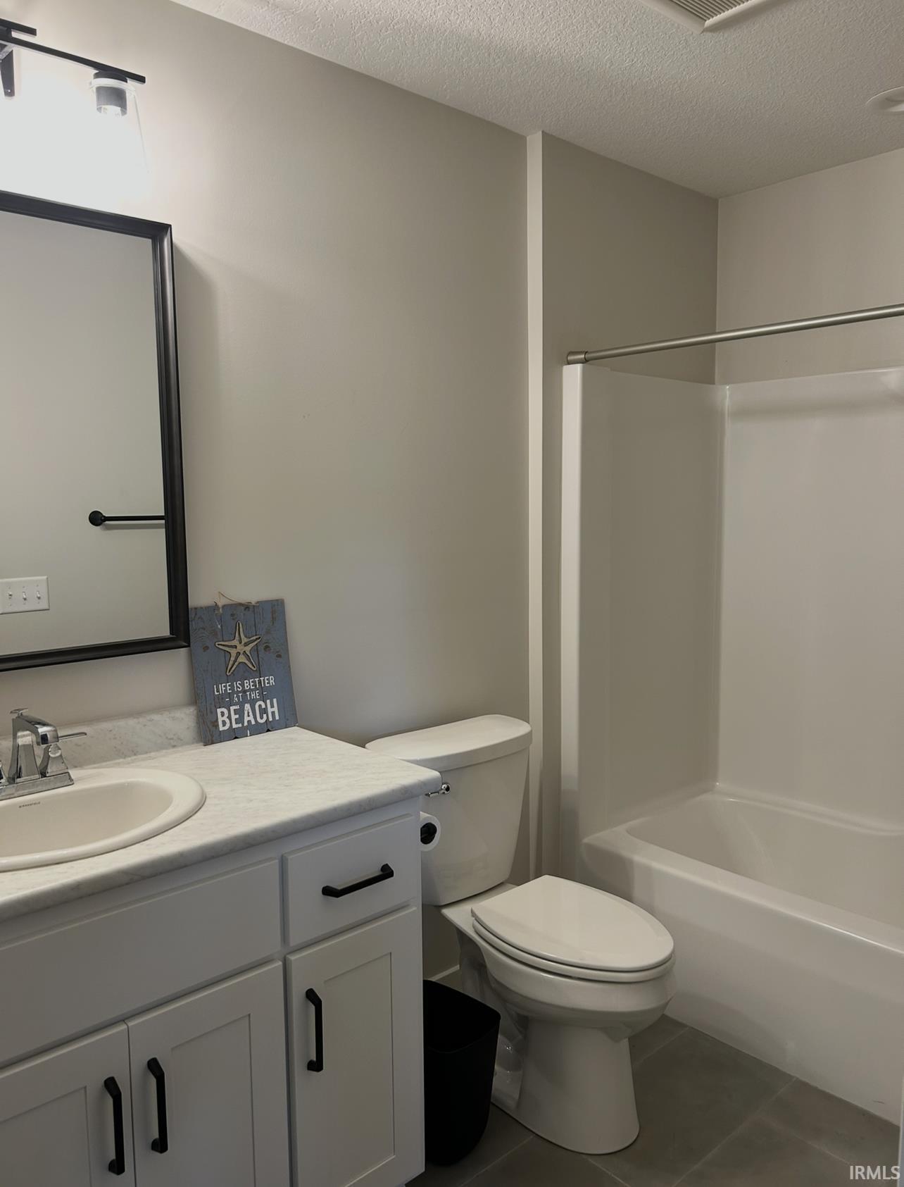 Full bathroom with vanity, a textured ceiling, dark tile patterned floors, and shower / bath combination