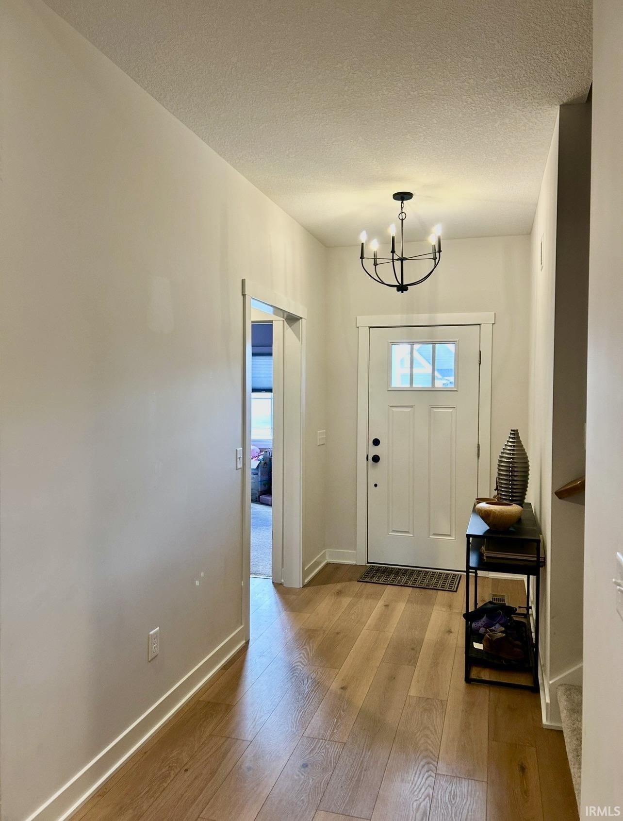 Foyer with light wood-style flooring, a textured ceiling, and a chandelier