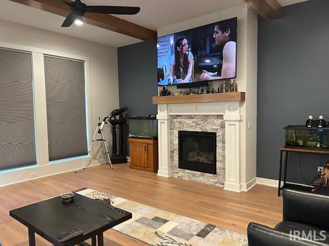 Living area with light wood finished floors, a ceiling fan, beamed ceiling, and a stone fireplace