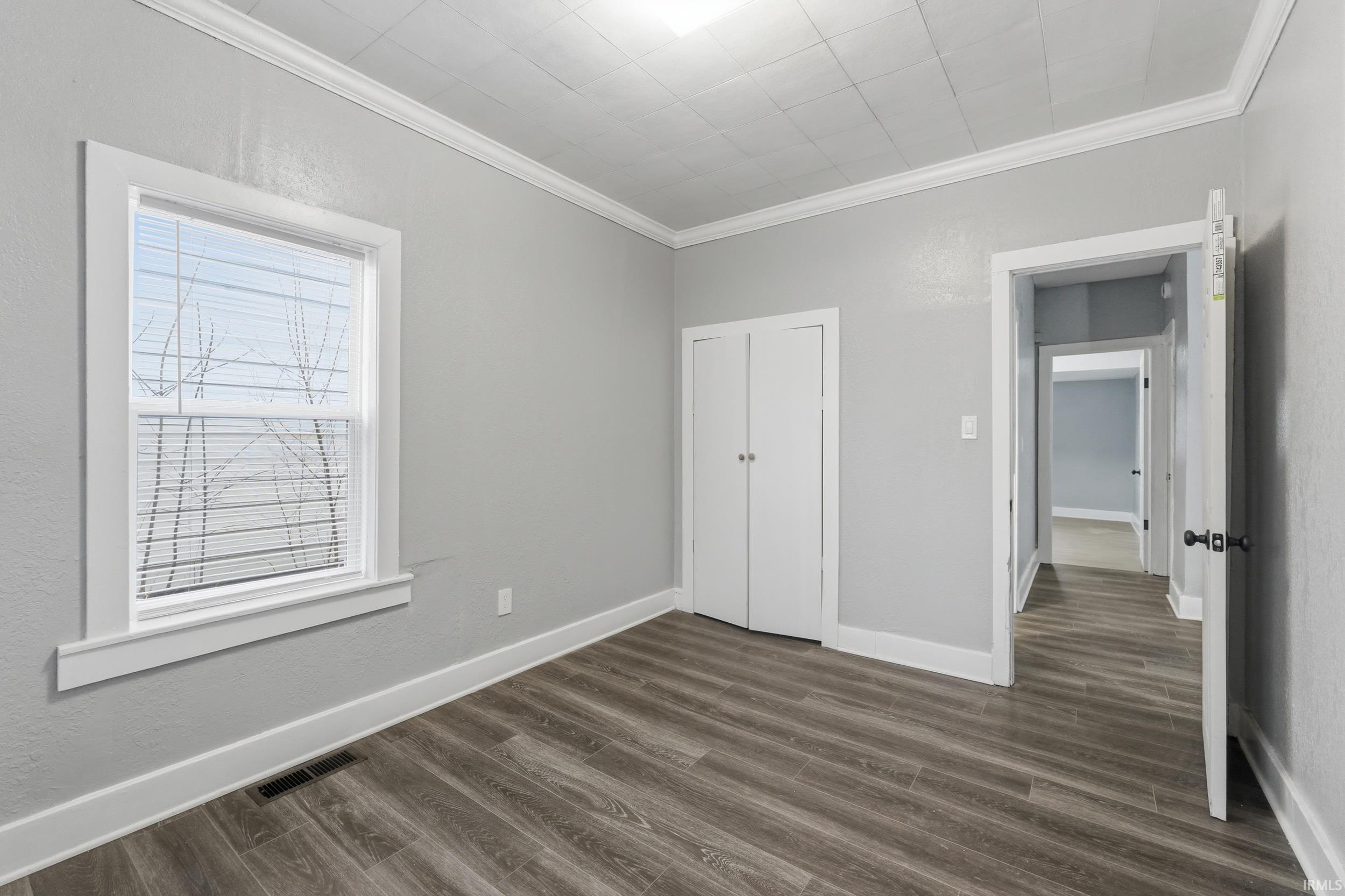 Unfurnished bedroom featuring ornamental molding and dark wood-type flooring