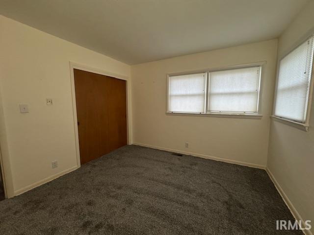 Unfurnished bedroom with dark carpet and a closet