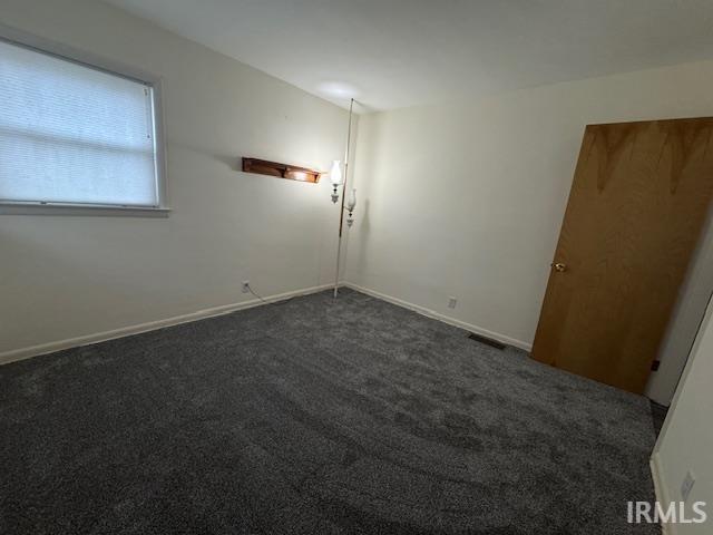Spare room featuring dark carpet and baseboards
