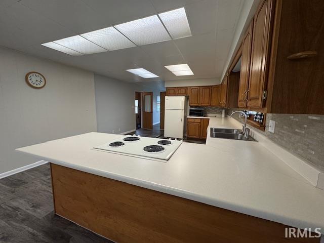 Kitchen featuring light countertops, a peninsula, wood finish cabinetry, white appliances, and decorative backsplash