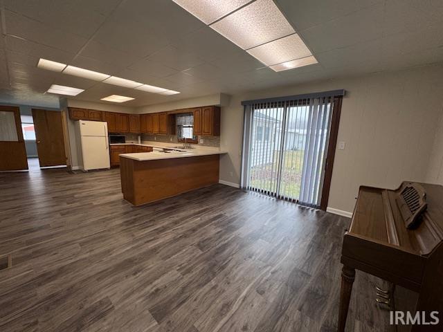 Kitchen with wood finish cabinetry, a peninsula, light countertops, freestanding refrigerator, and dark wood finished floors