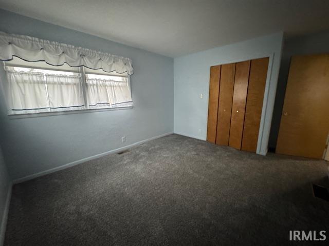Unfurnished bedroom featuring dark colored carpet and a closet