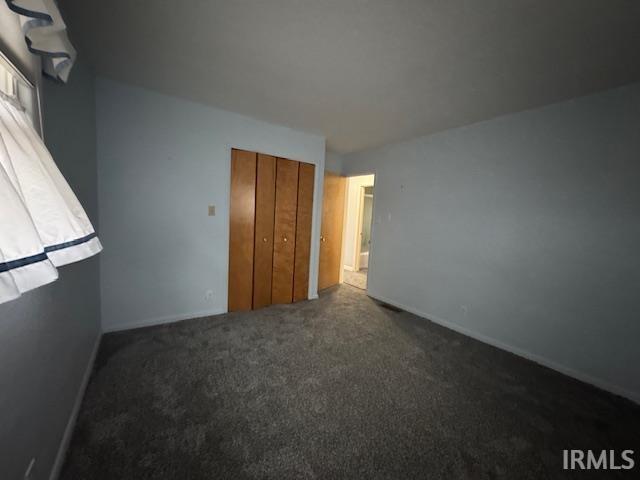 Unfurnished bedroom featuring dark carpet and a closet