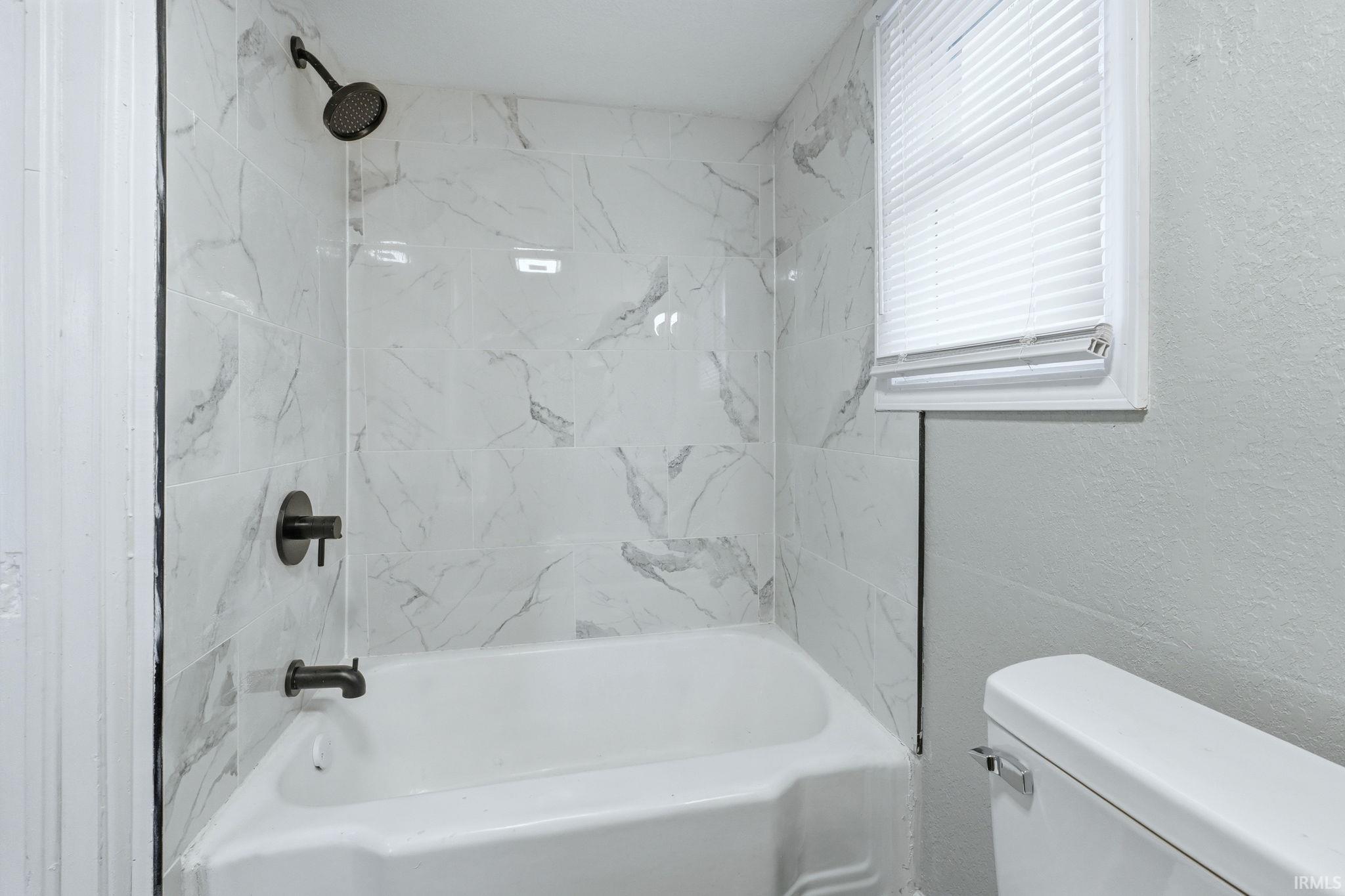 Full bath with bathing tub / shower combination and a textured wall
