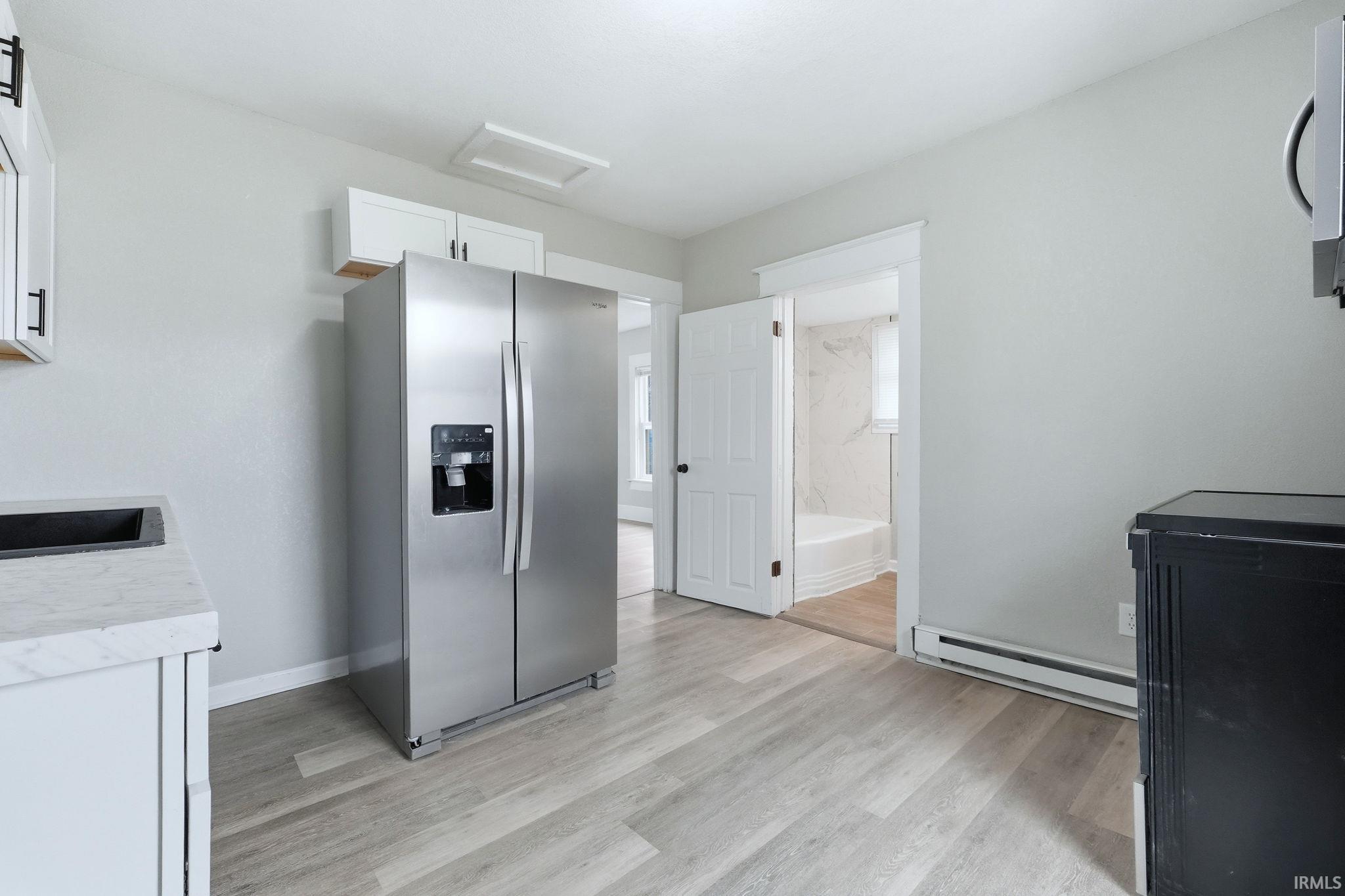 Kitchen featuring stainless steel refrigerator with ice dispenser, light countertops, a baseboard radiator, white cabinets, and light wood finished floors