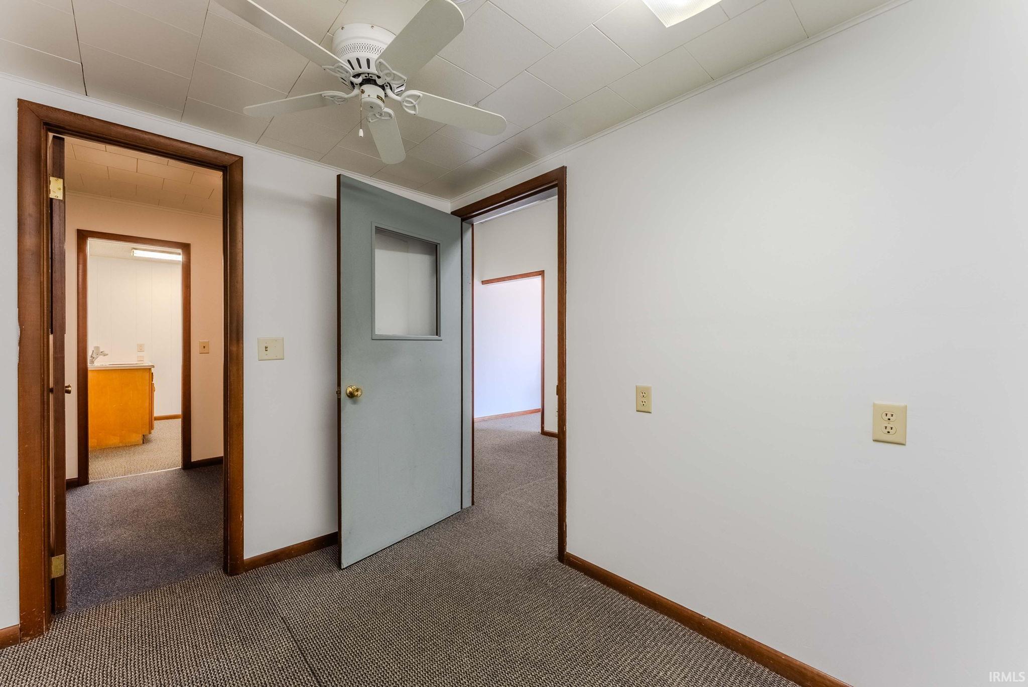 Unfurnished bedroom featuring dark colored carpet, a ceiling fan, and crown molding