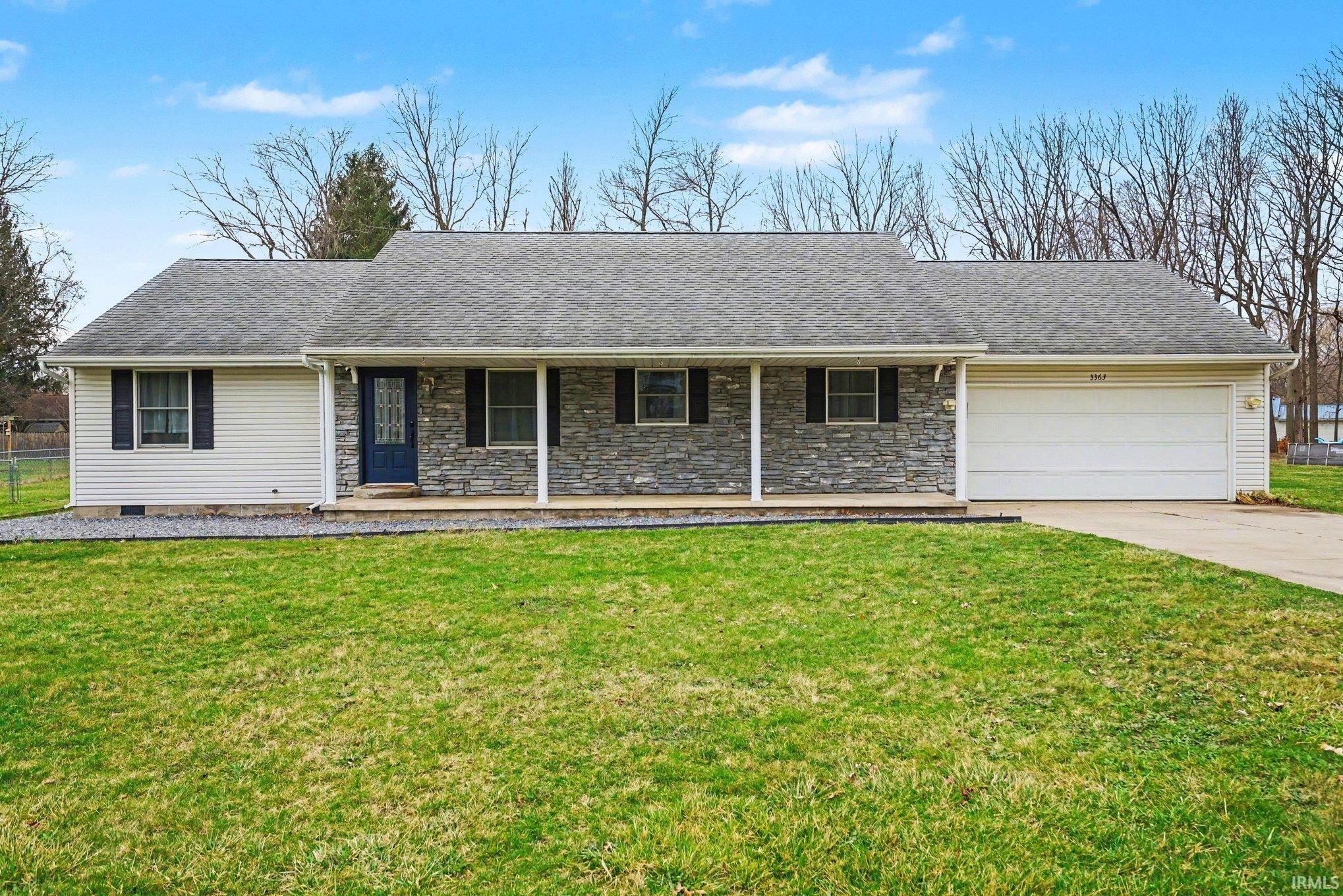 Ranch-style home with an attached garage, a porch, a front lawn, driveway, and a shingled roof
