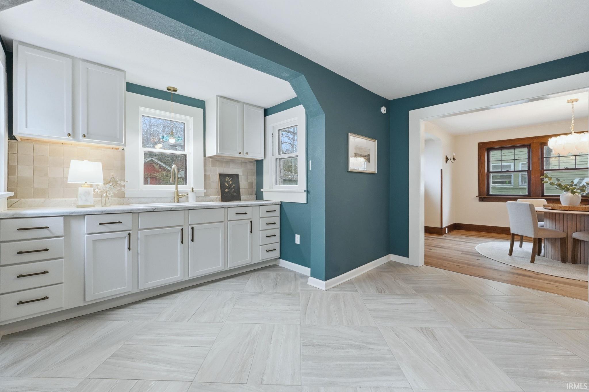 Kitchen with hanging light fixtures, white cabinets, and tasteful backsplash