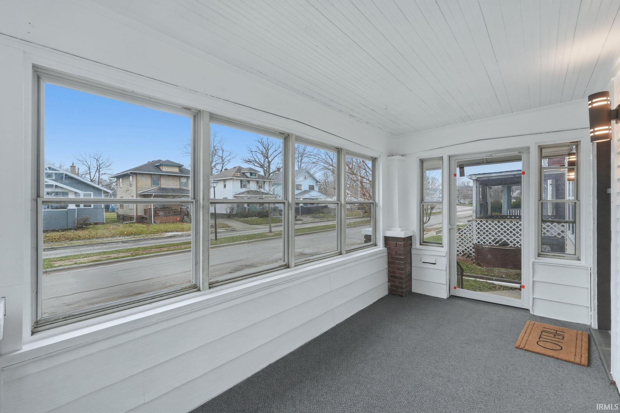 Unfurnished sunroom featuring carpet flooring, wooden ceiling, and a residential view