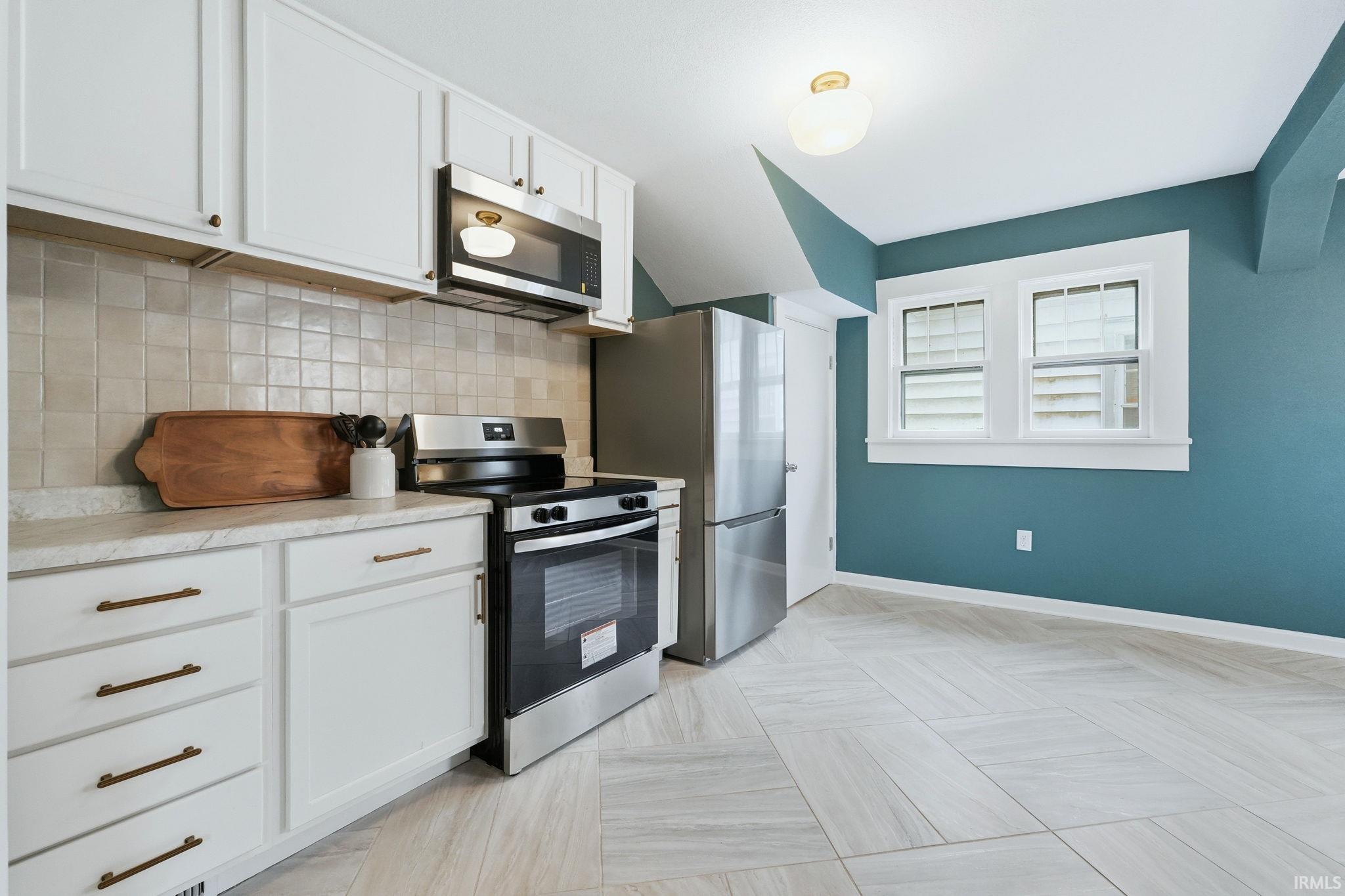Kitchen featuring stainless steel appliances, light countertops, white cabinets, and decorative backsplash