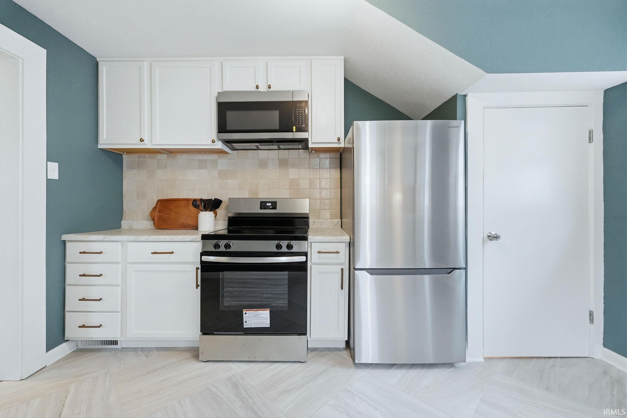 Kitchen with stainless steel appliances, white cabinetry, and backsplash
