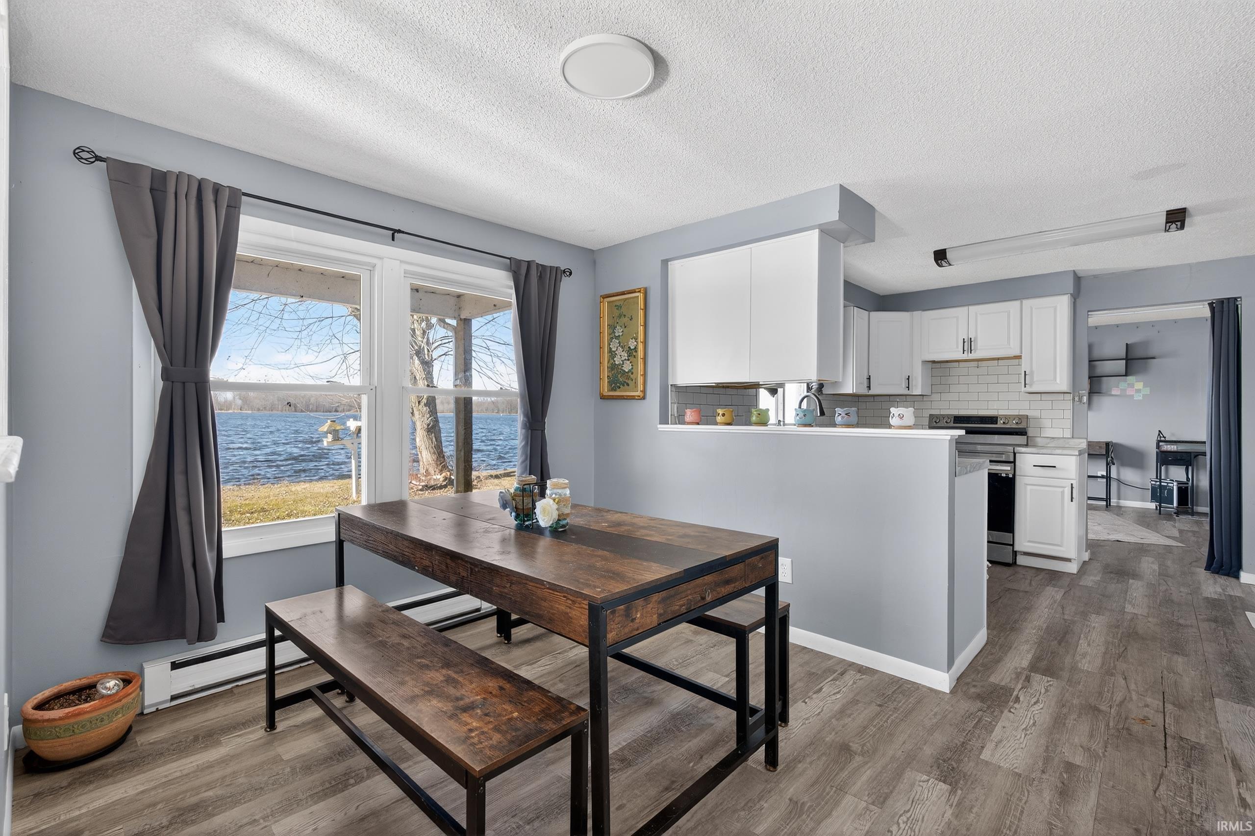 Dining room with a water view, light wood-style floors, a baseboard radiator, and a textured ceiling
