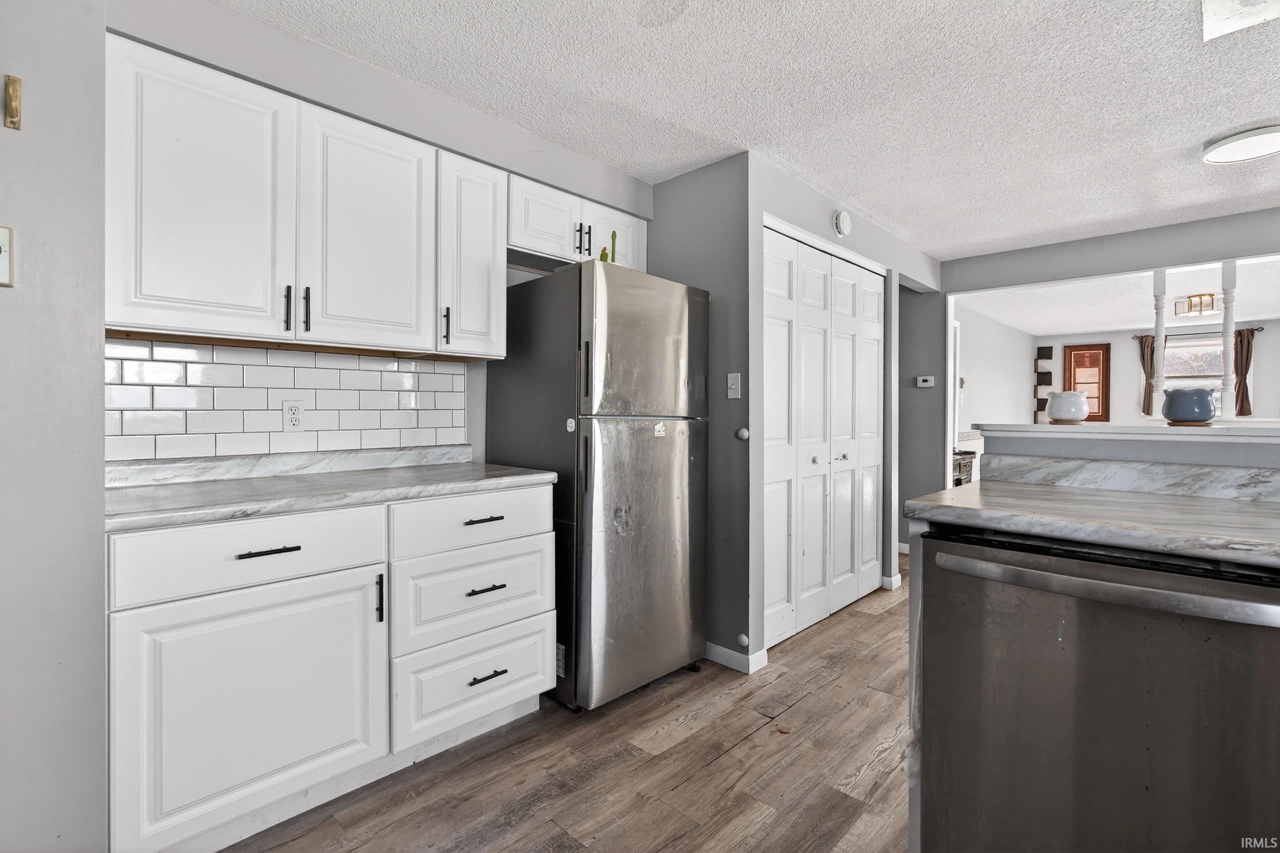 Kitchen featuring stainless steel appliances, white cabinetry, a textured ceiling, dark wood finished floors, and tasteful backsplash