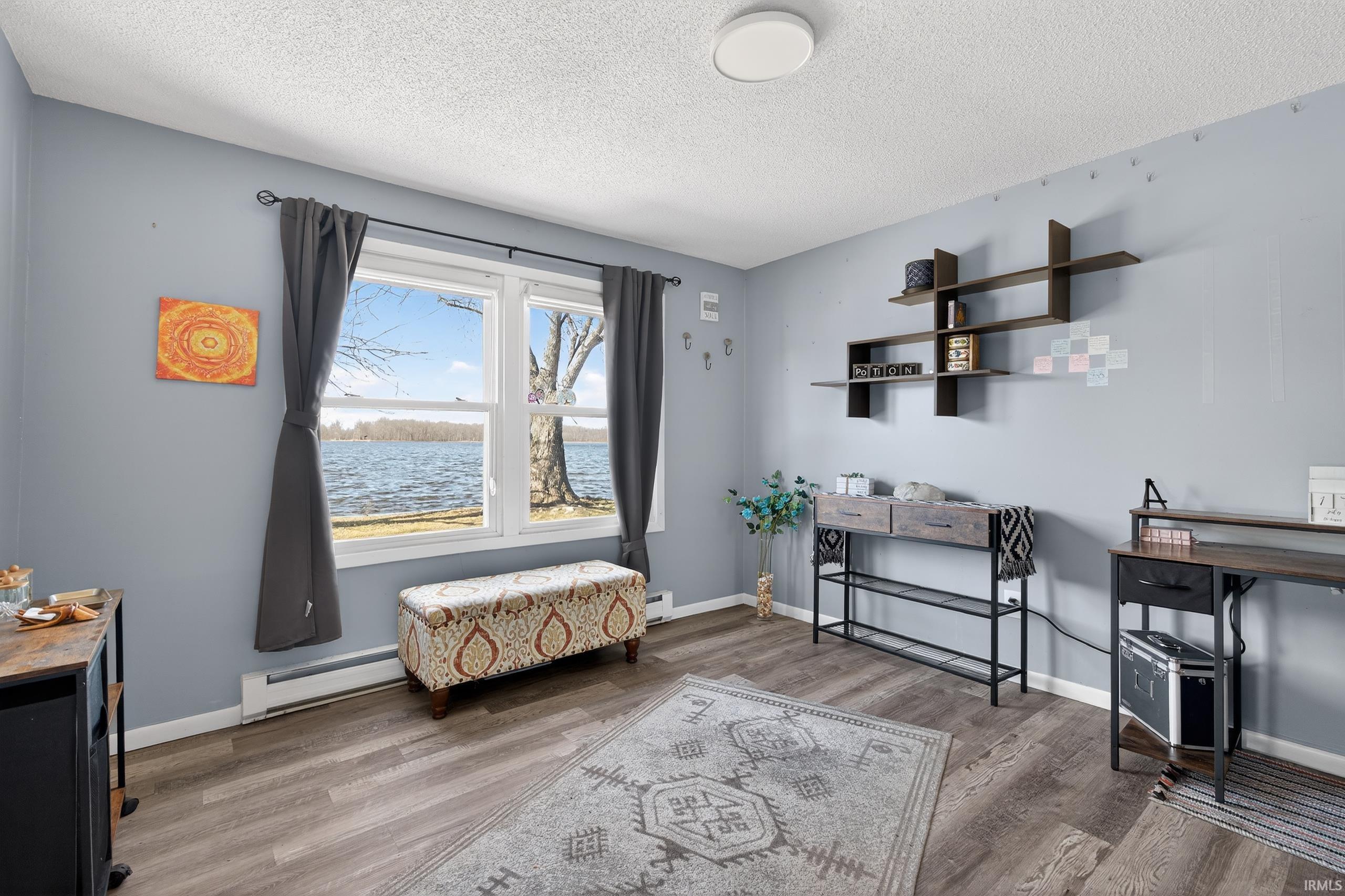 Den featuring a baseboard radiator, light wood-style floors, a water view, a textured ceiling, and baseboard heating