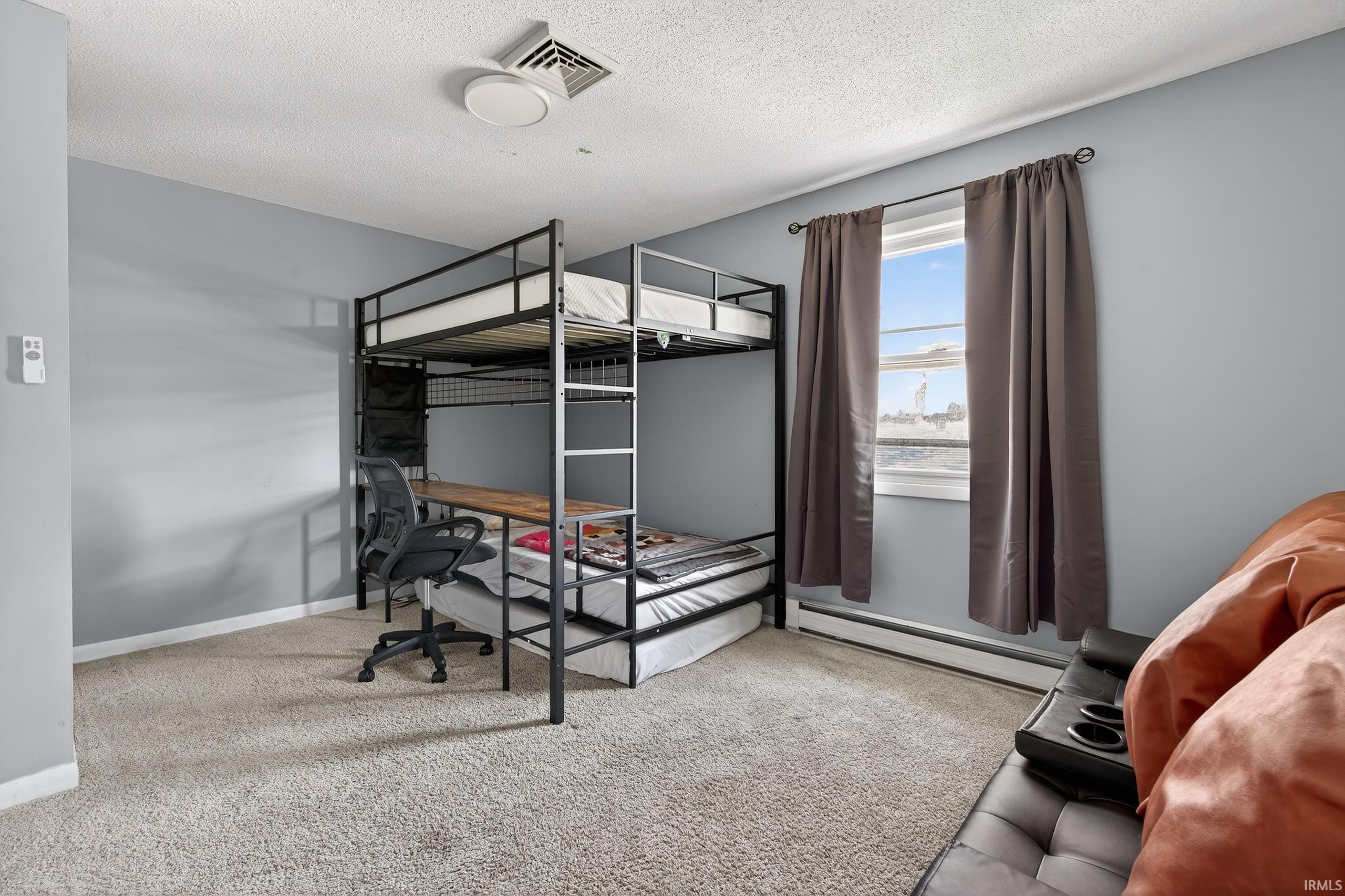 Bedroom with light carpet, baseboard heating, a textured ceiling, and an office area