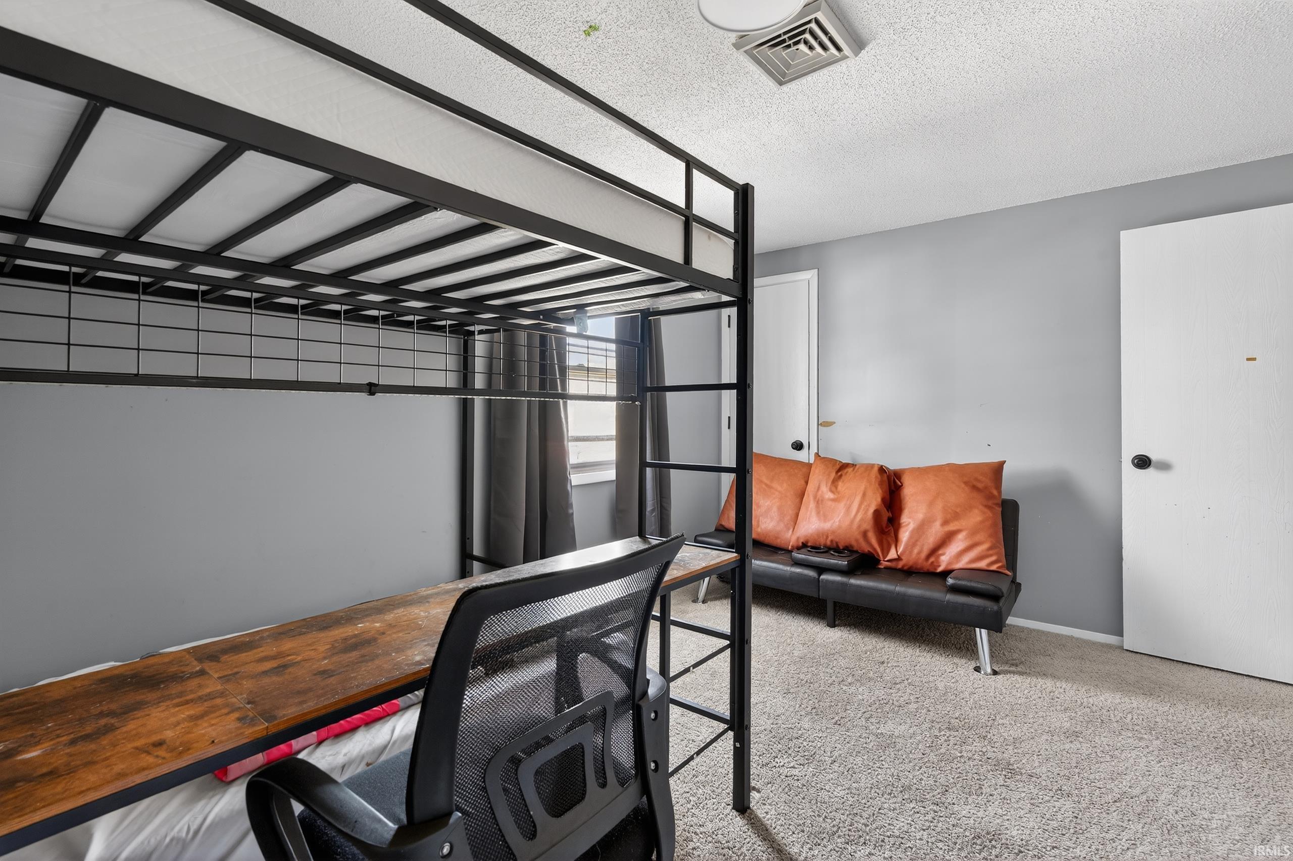 Bedroom featuring a desk, light carpet, and a textured ceiling