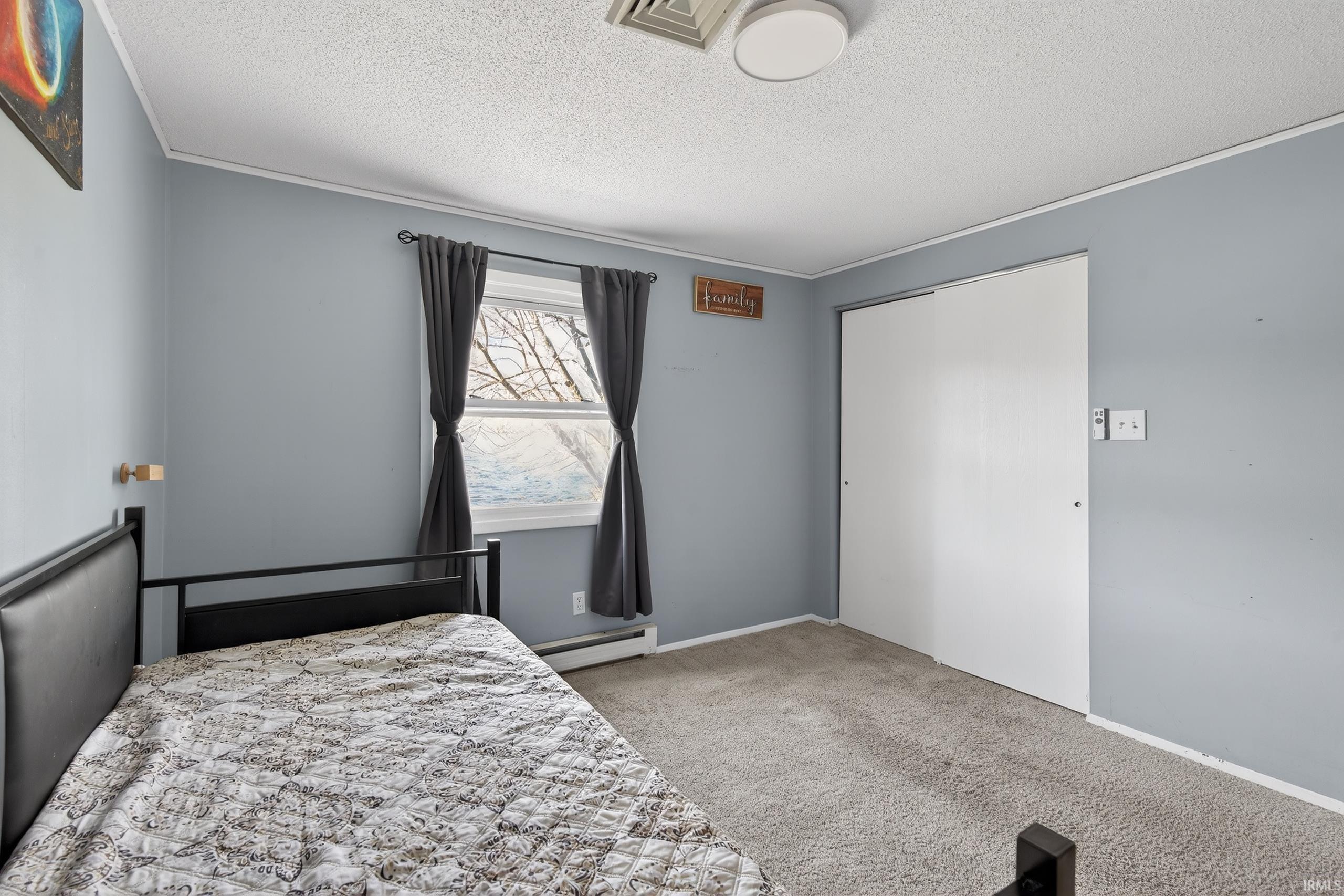 Bedroom featuring light carpet, a textured ceiling, a closet, and a baseboard radiator