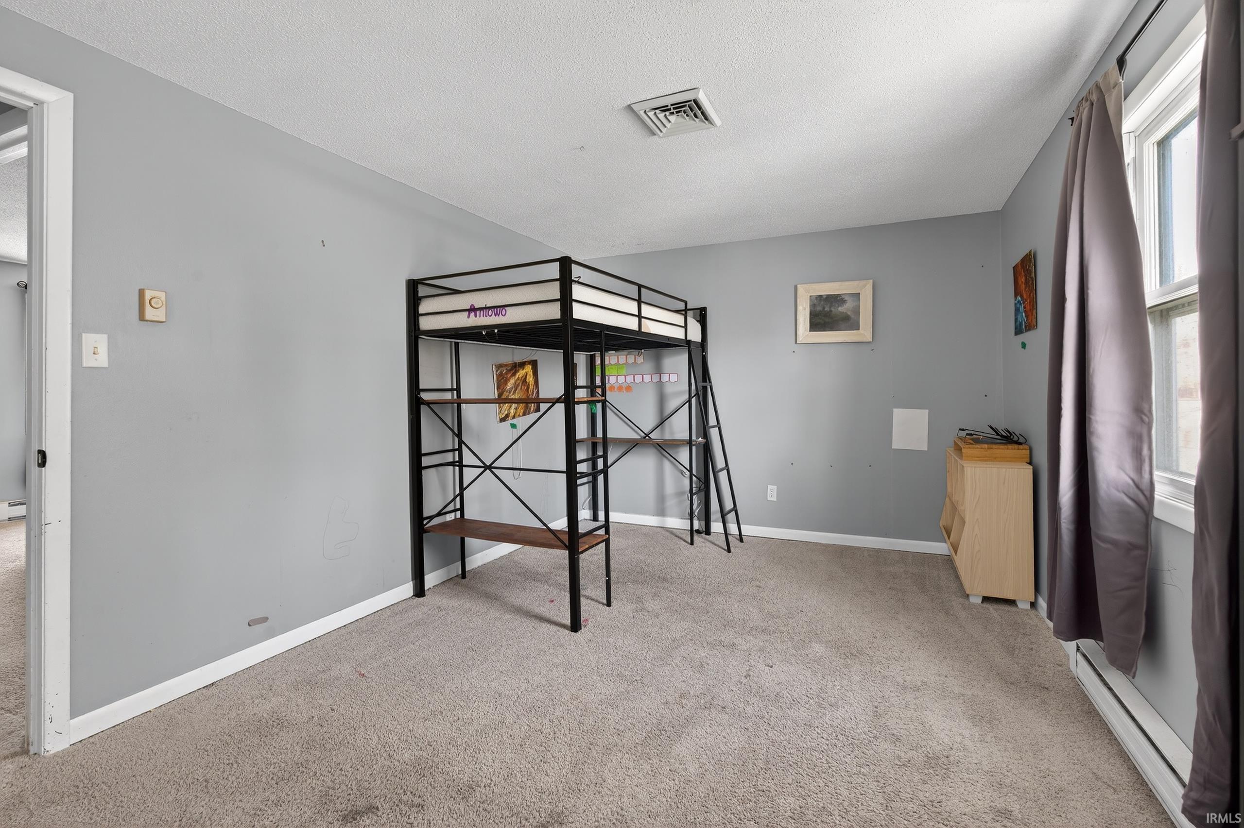 Unfurnished bedroom featuring a baseboard heating unit, light carpet, and a textured ceiling