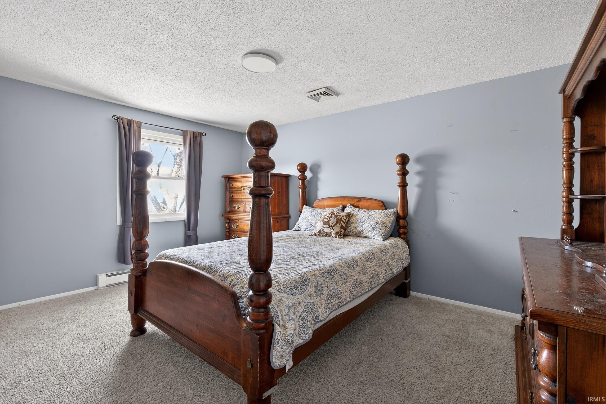 Bedroom with light colored carpet, a textured ceiling, and a baseboard radiator