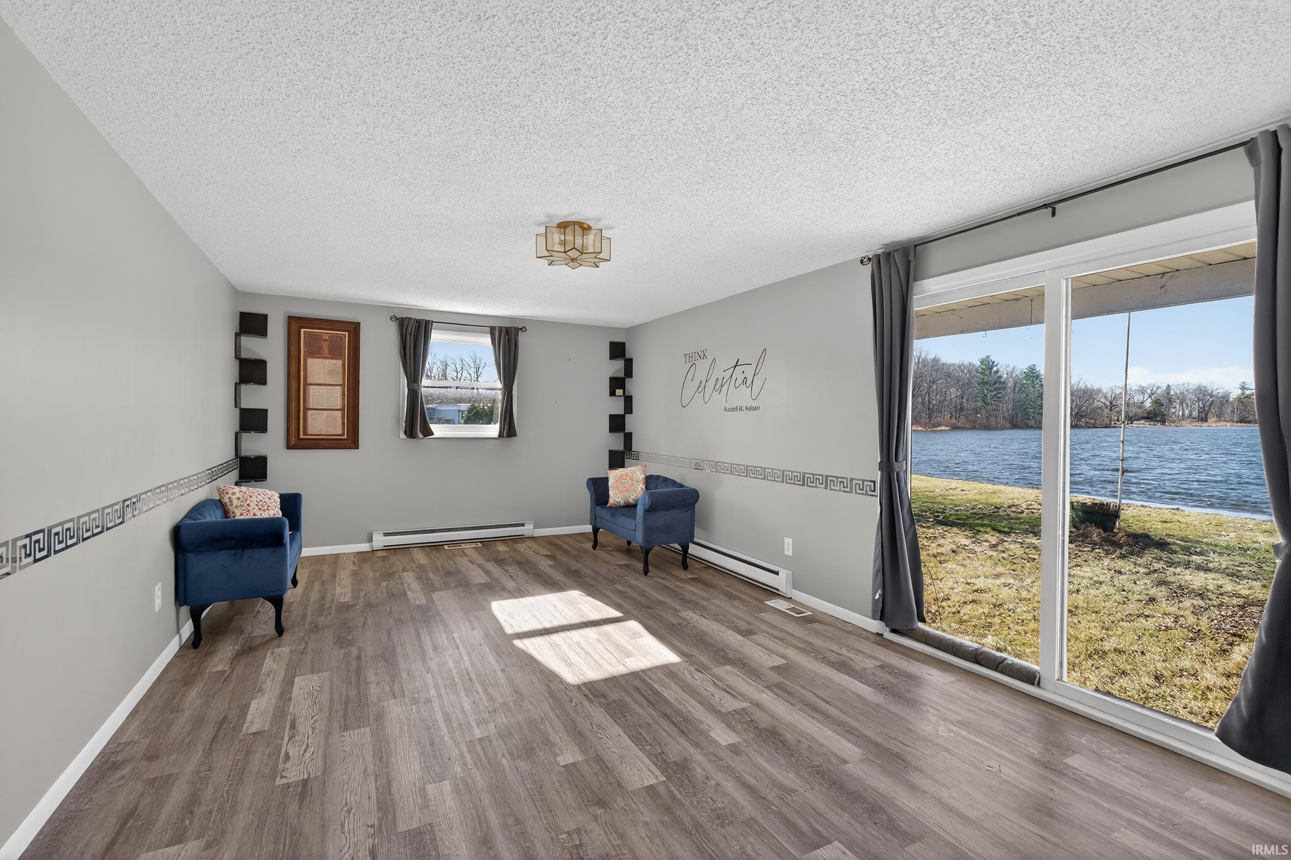 Family room featuring wood finished floors, baseboard heating, a textured ceiling, a water view, and a baseboard radiator
