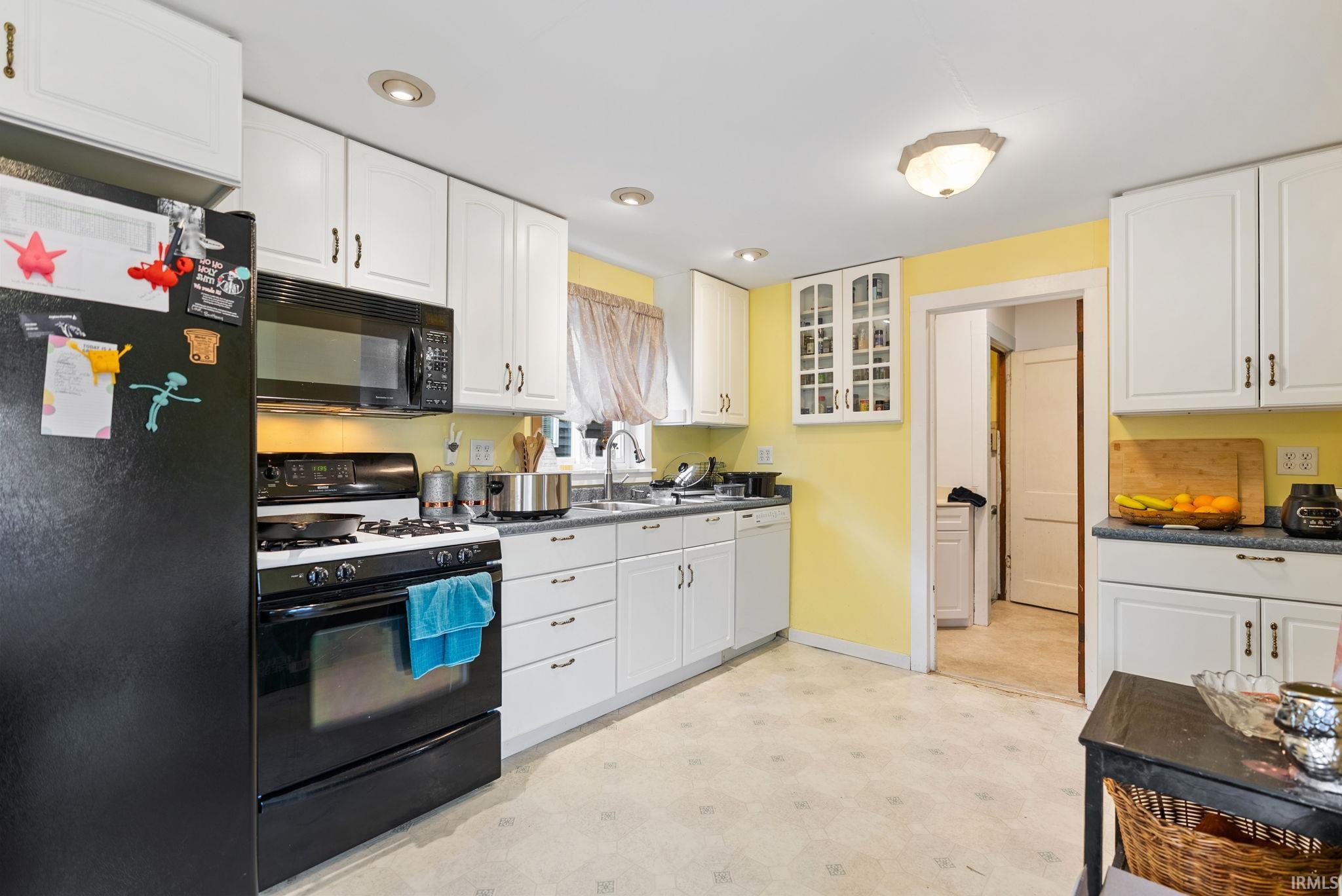 Kitchen featuring black appliances, light flooring, glass fronted cabinets, white cabinets, and recessed lighting