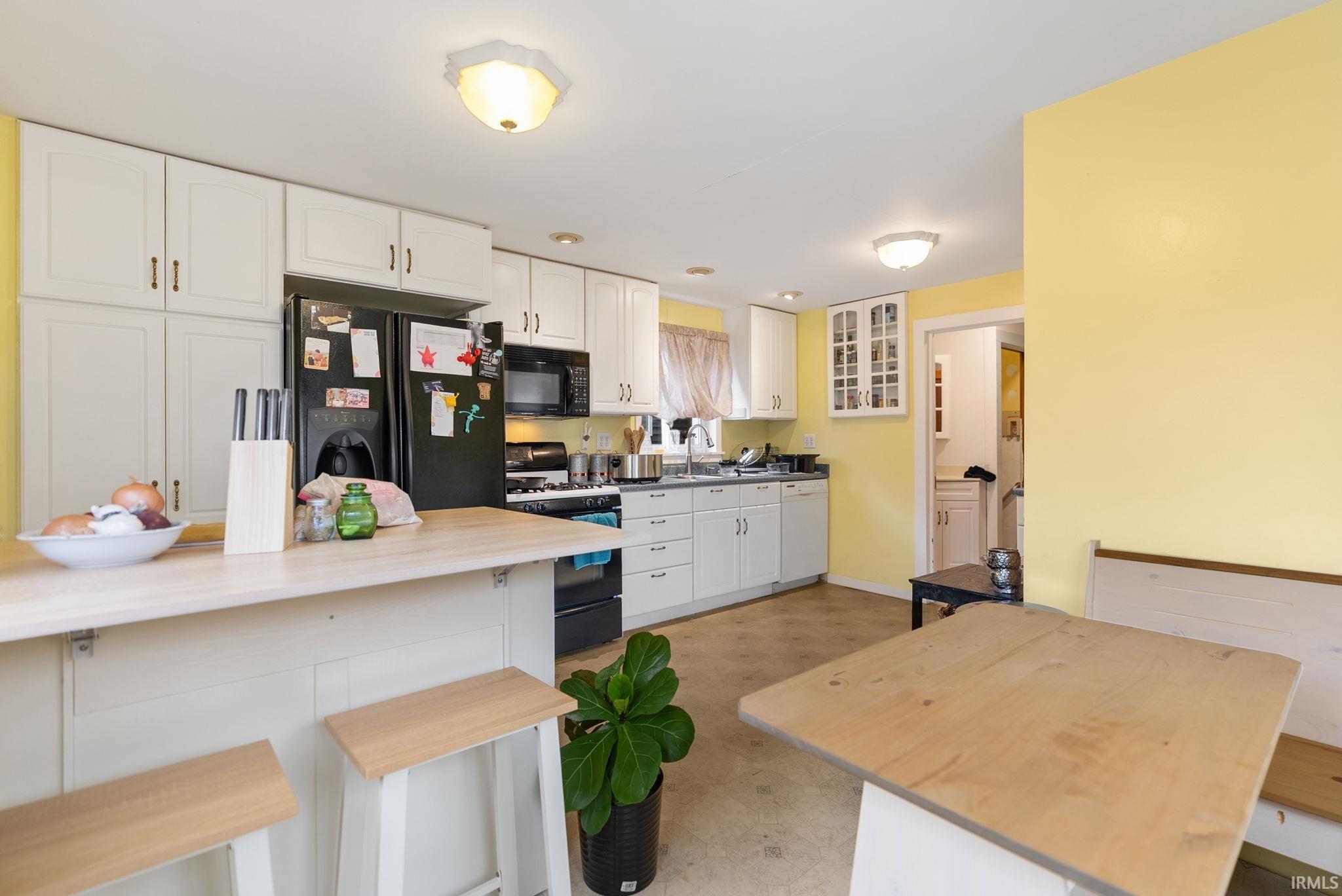 Kitchen with a breakfast bar area, white cabinetry, wooden counters, black appliances, and light floors