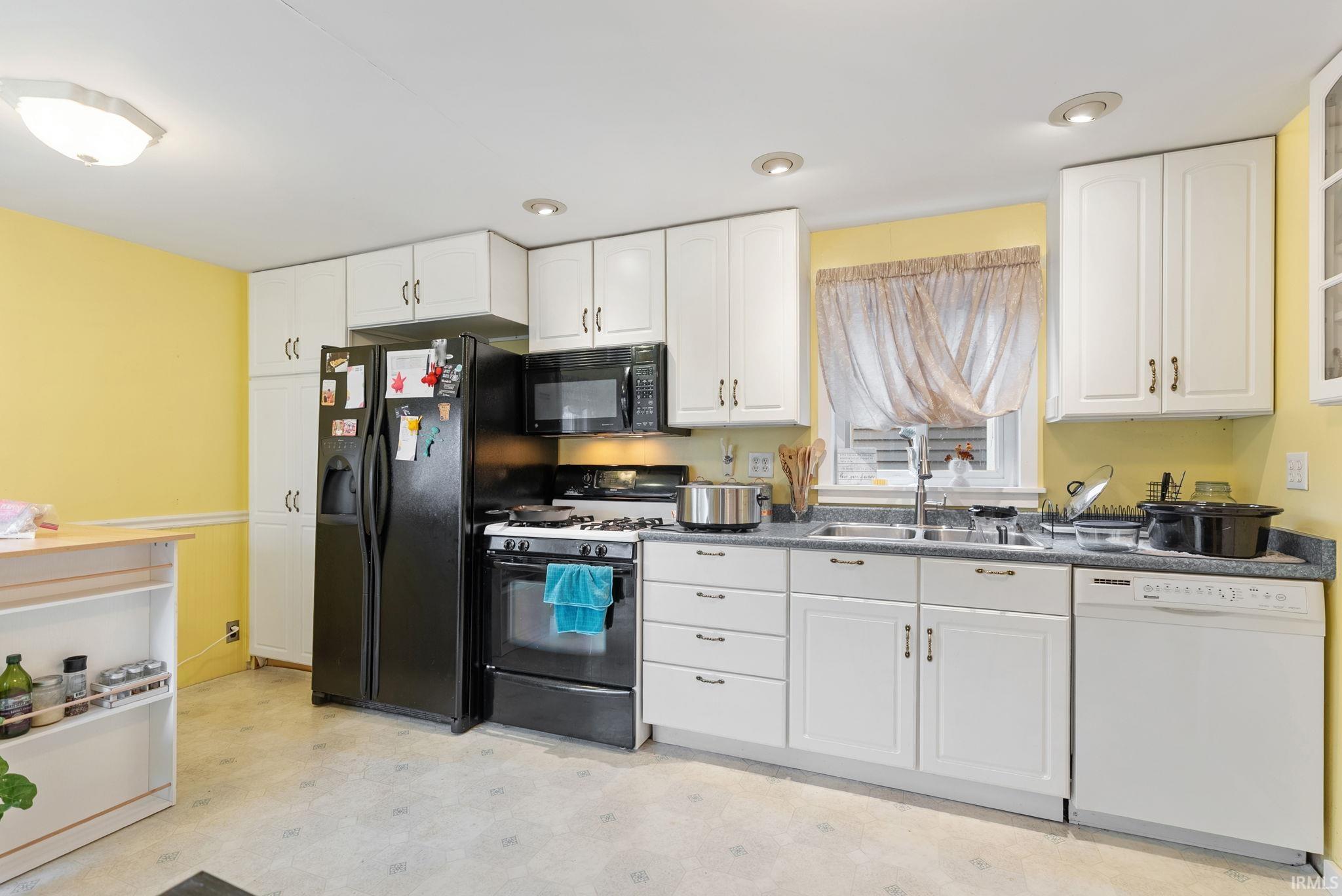 Kitchen featuring light flooring, range with gas cooktop, white dishwasher, dark countertops, and white cabinetry