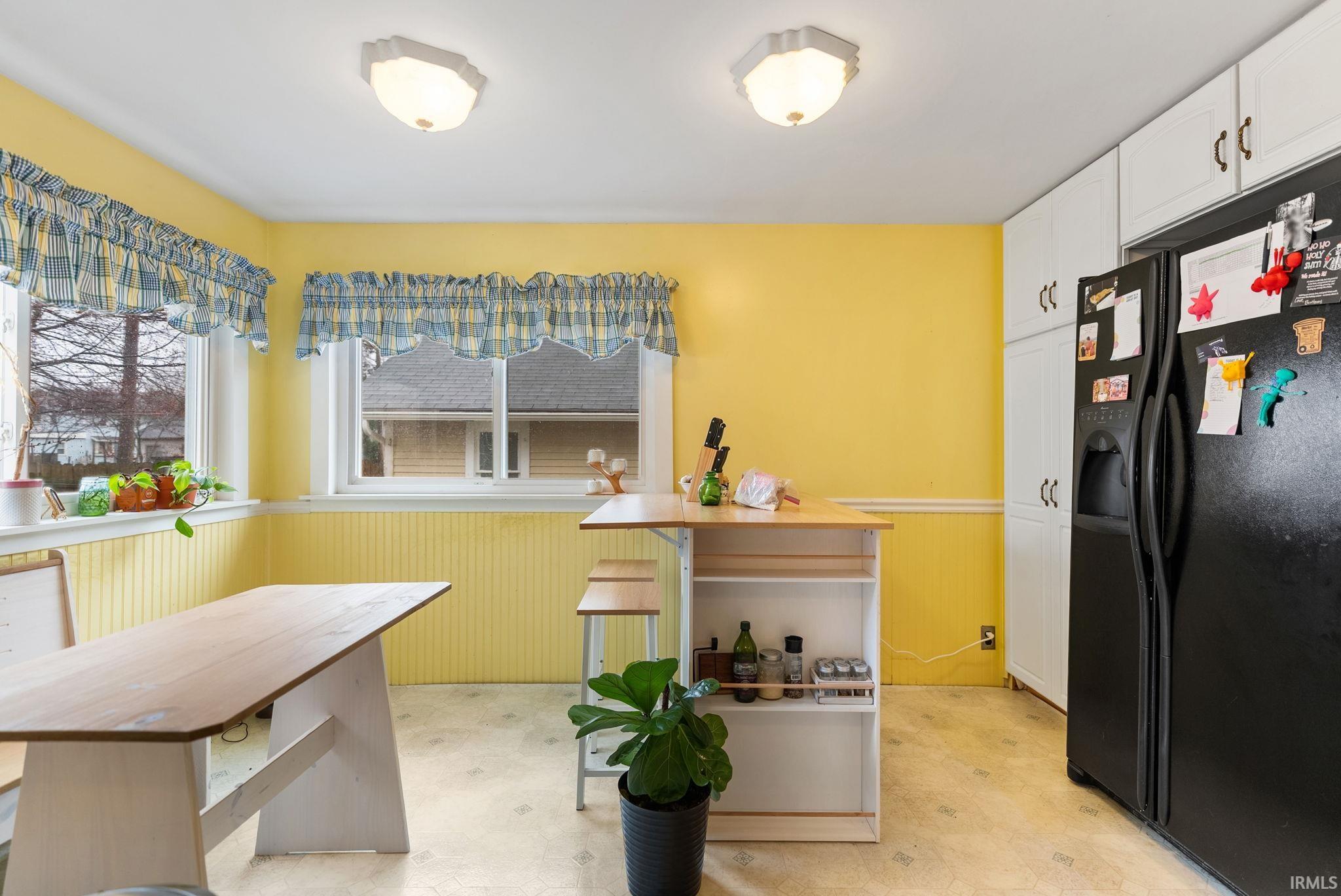 Kitchen with a wainscoted wall, light floors, black fridge with ice dispenser, white cabinetry, and wood walls
