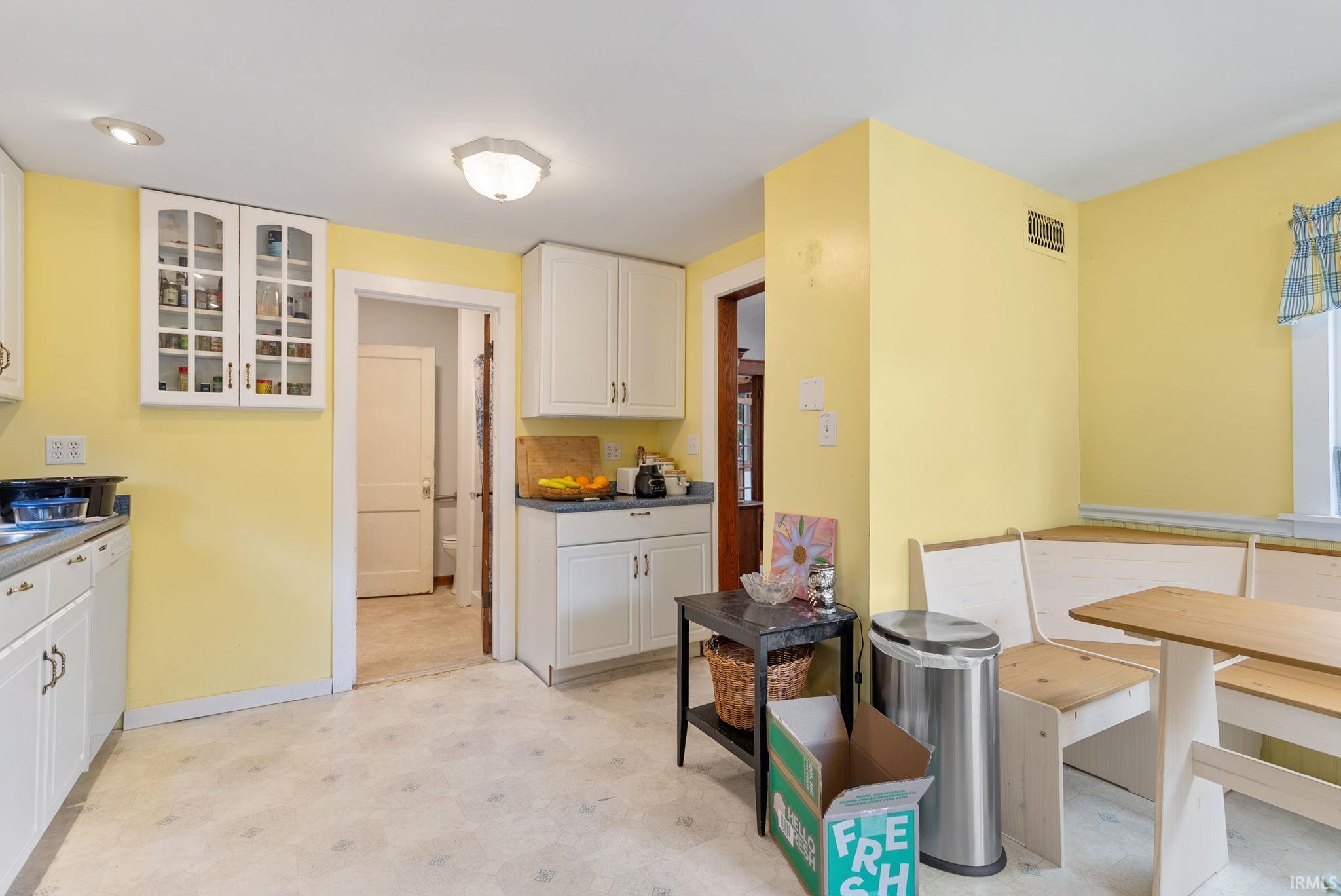 Kitchen with light flooring, glass fronted cabinets, white cabinetry, dark countertops, and white dishwasher